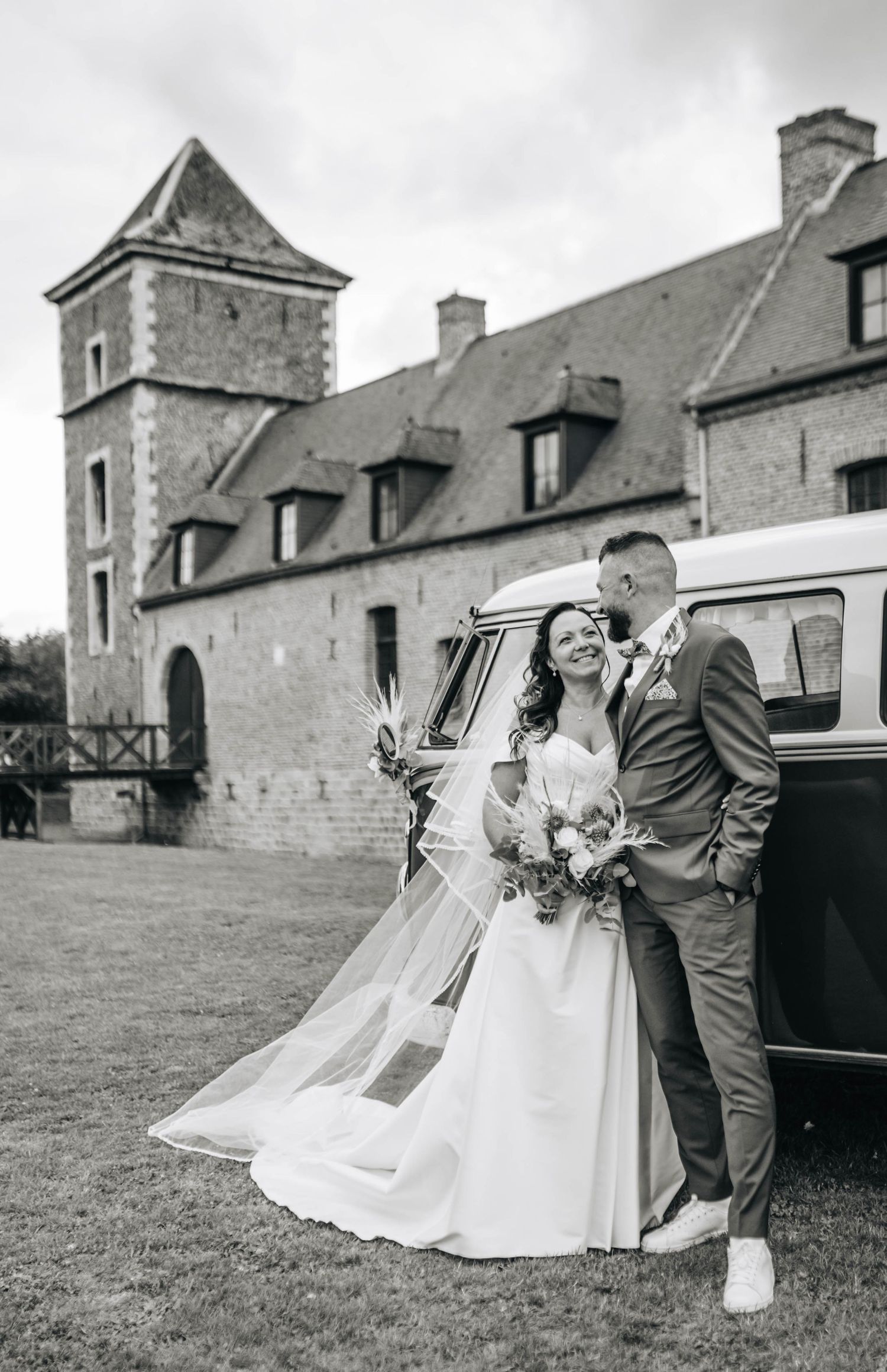 Wedding couple posing near vintage buildings and classic car in black and white photography.