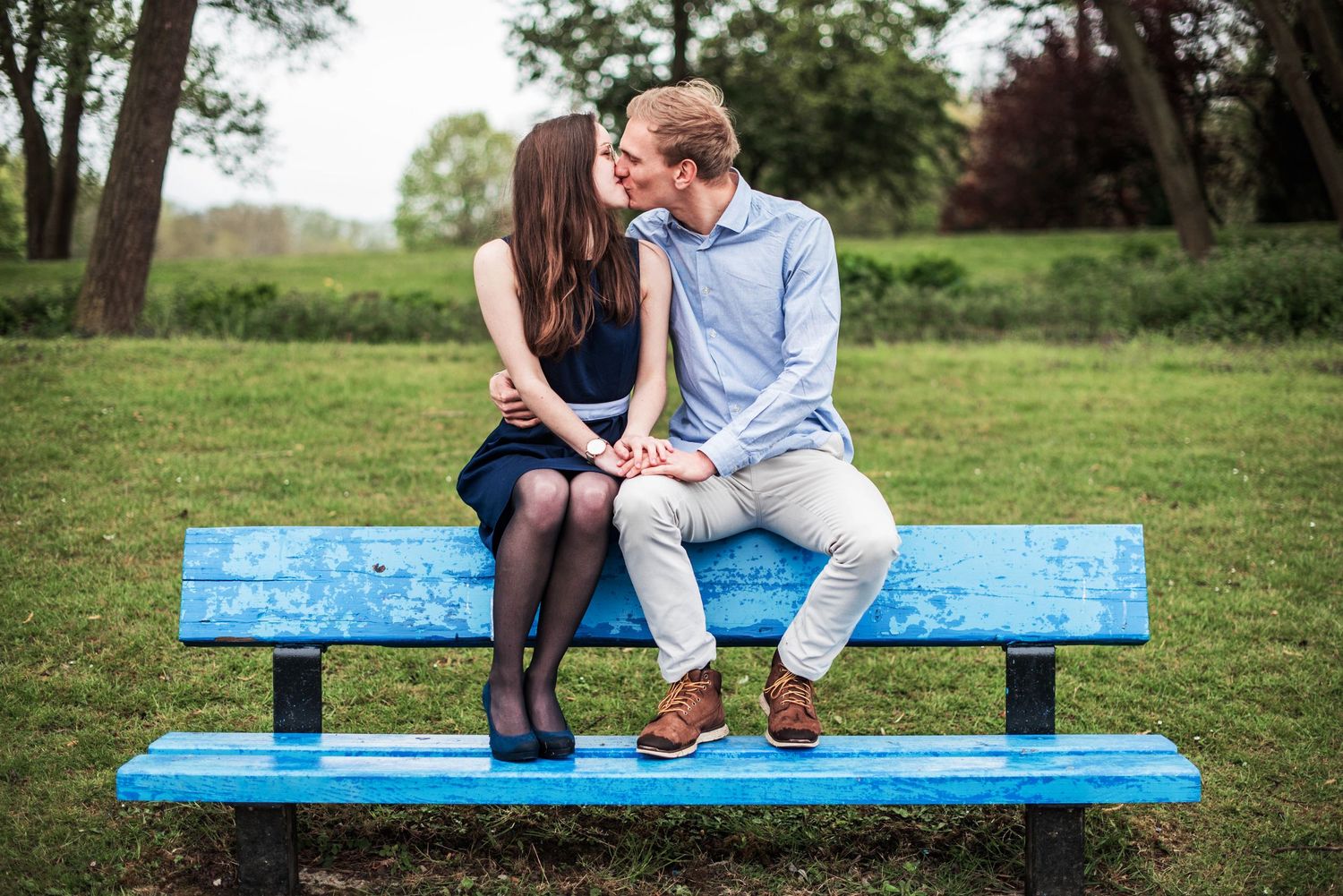 Couple sharing intimate moment on blue park bench surrounded by trees.