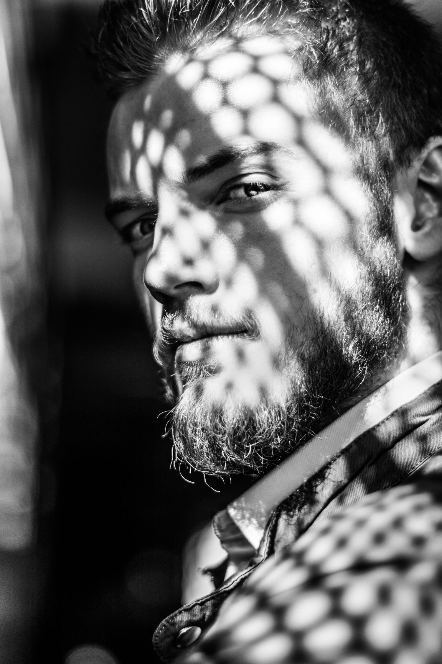 Artistic black and white portrait with honeycomb shadow pattern overlay.