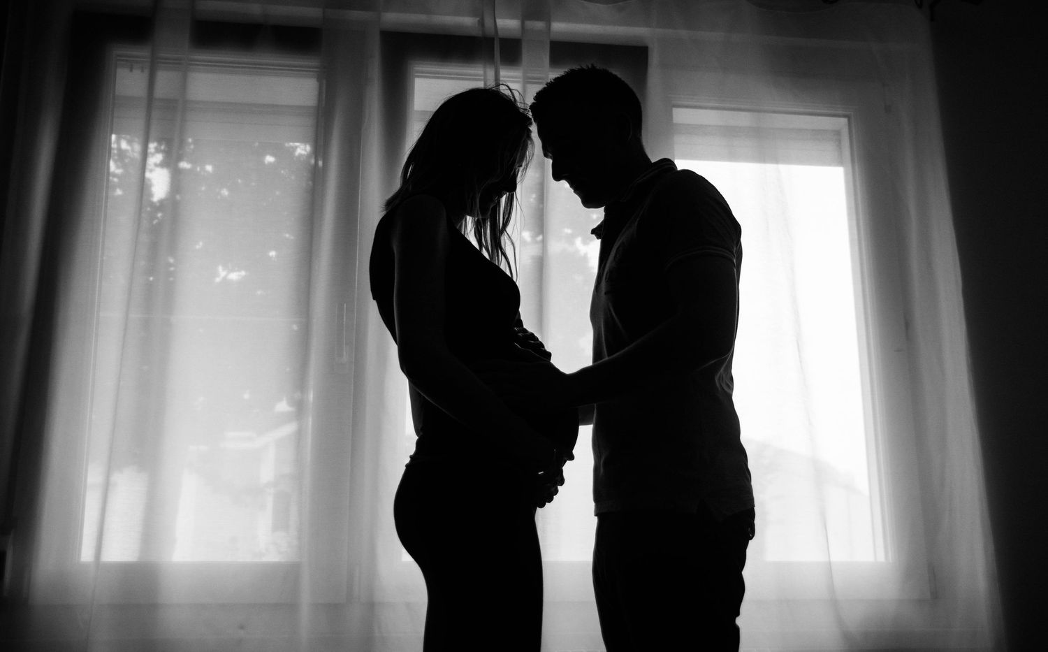 Silhouetted couple poses together against bright window light in romantic black and white series.