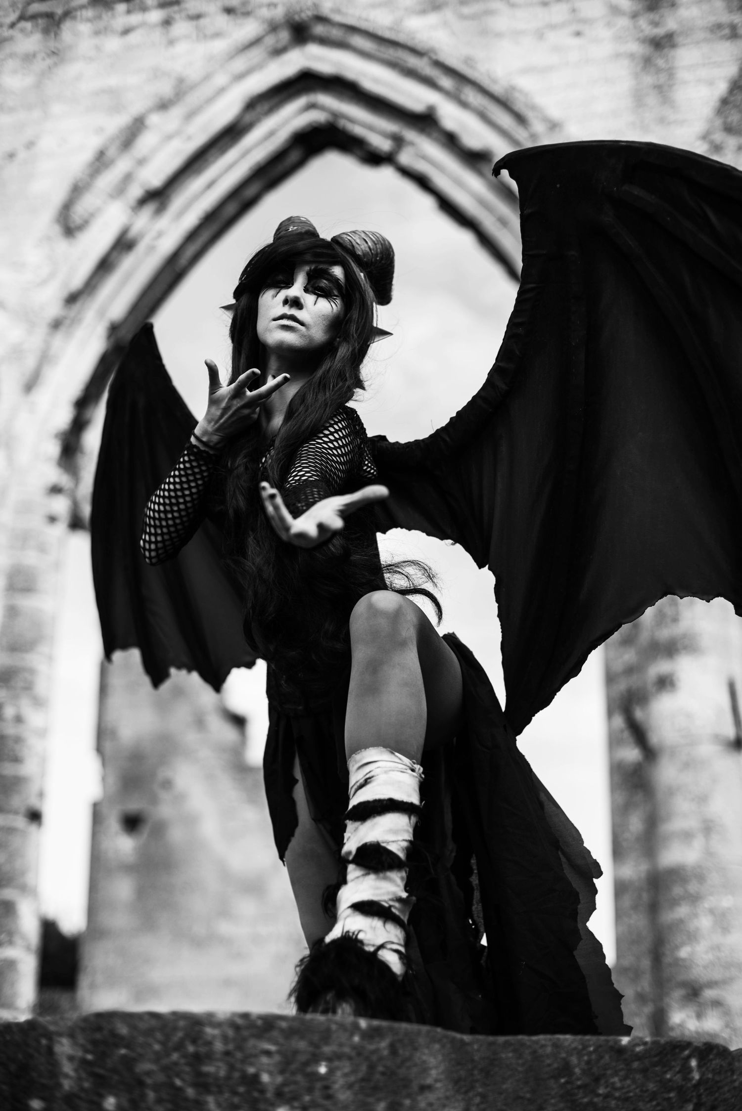 Dramatic black and white photos of figure with bat wings posing against stone archways.