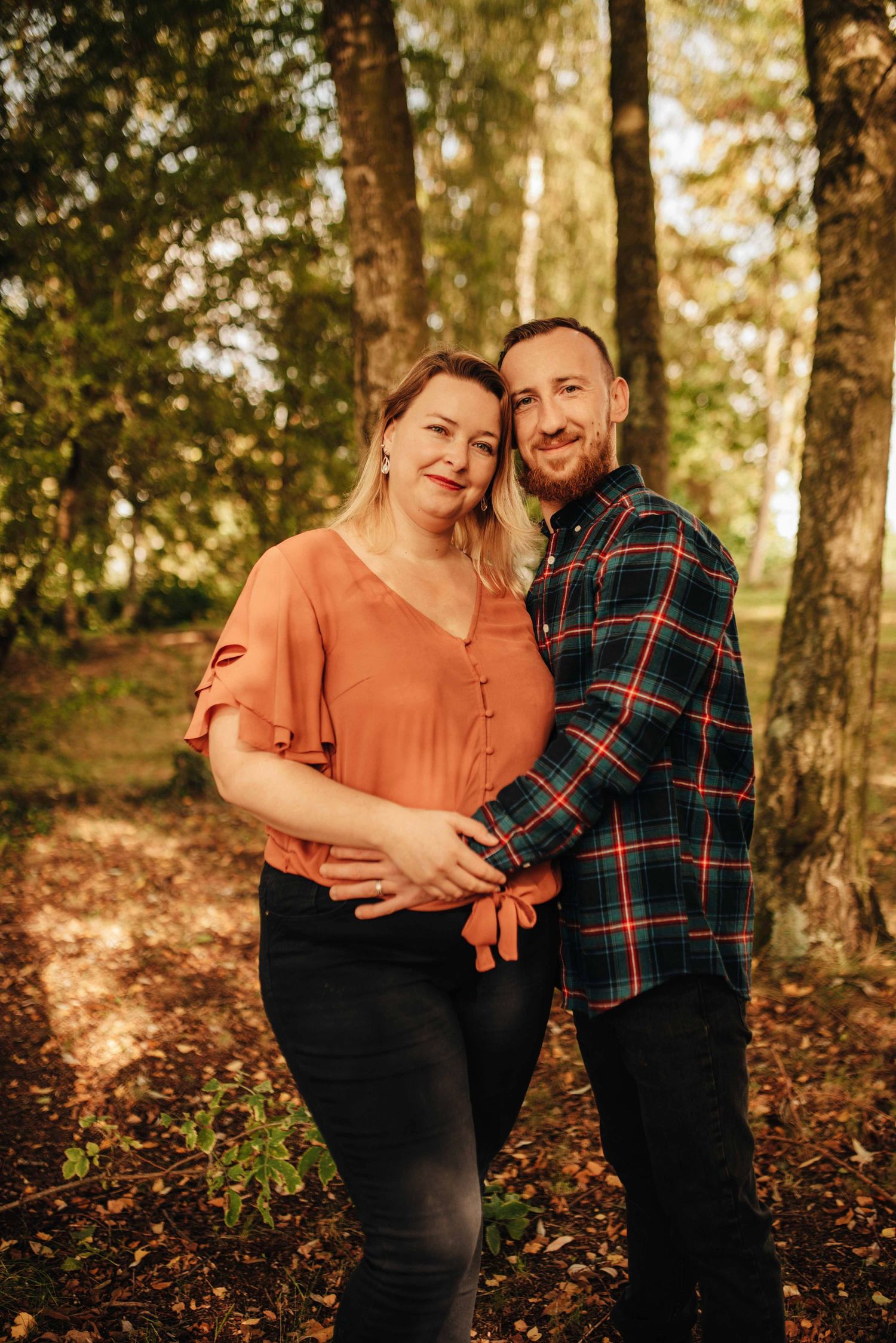 A couple shares laughter in a sunlit autumn forest setting.