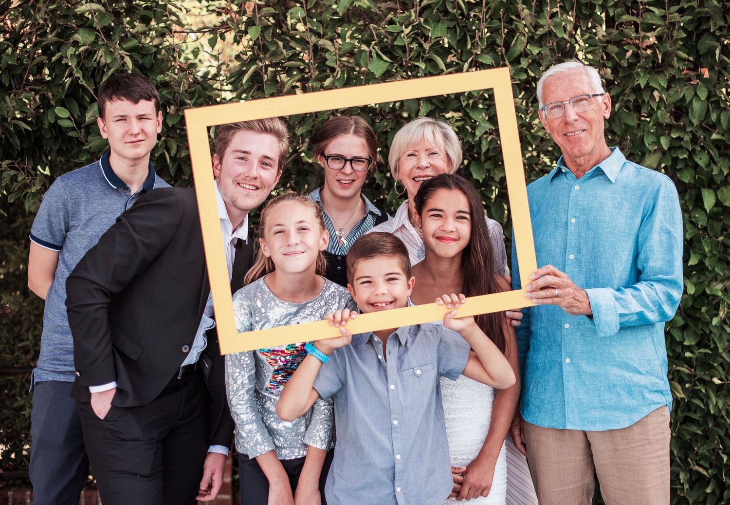 Family members posing with a large golden picture frame in an outdoor setting.
