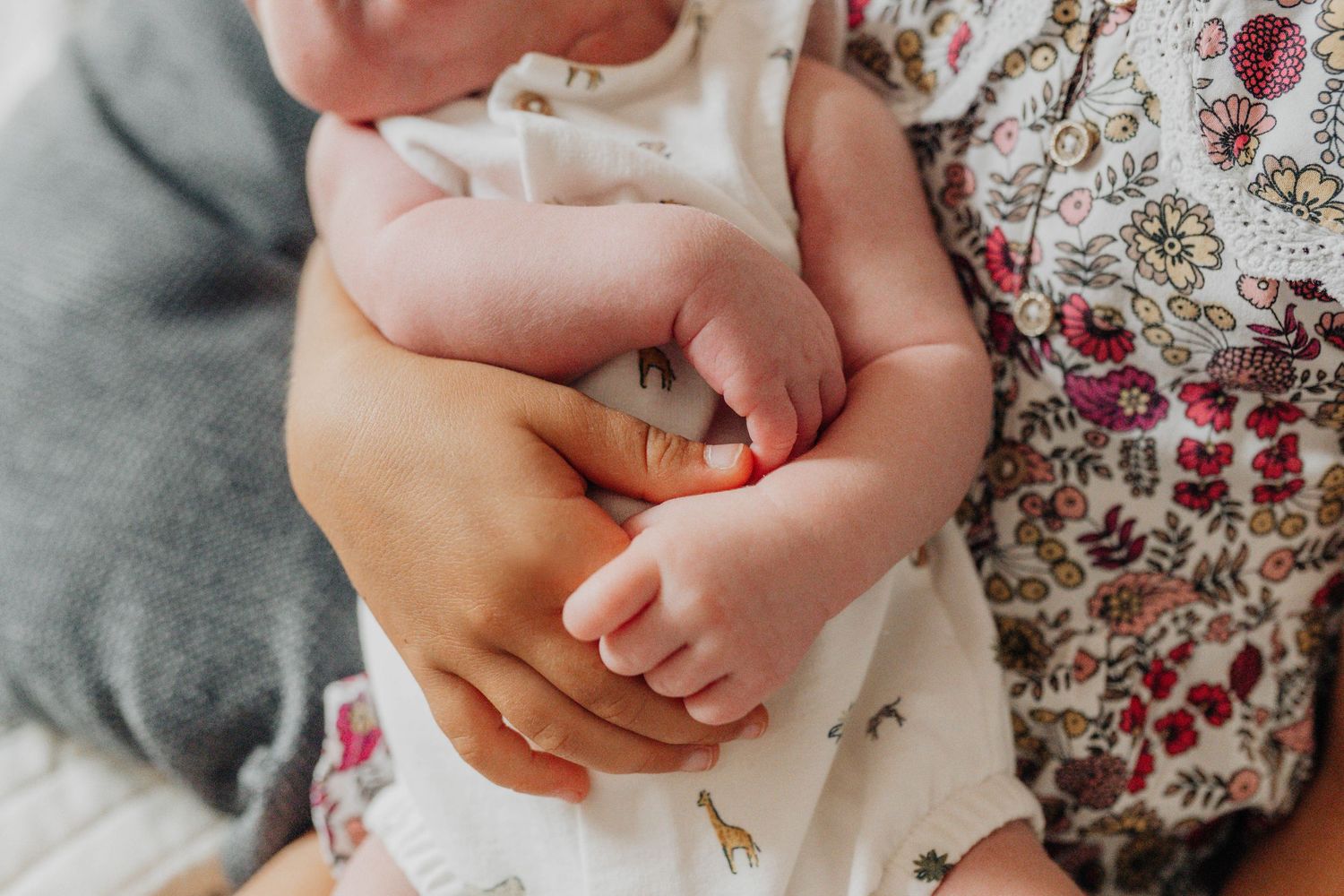 Close-up of tiny baby hands grasping against a floral patterned background.