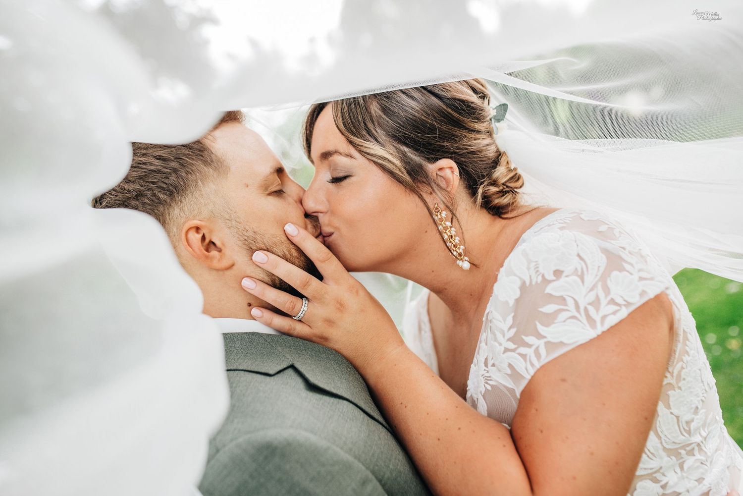 Romantic wedding photo of couple sharing intimate kiss under flowing veil.