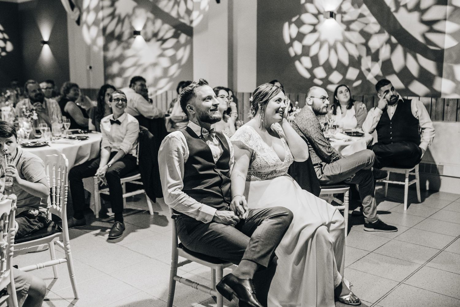 Black and white reception scene shows guests seated at decorated indoor venue.