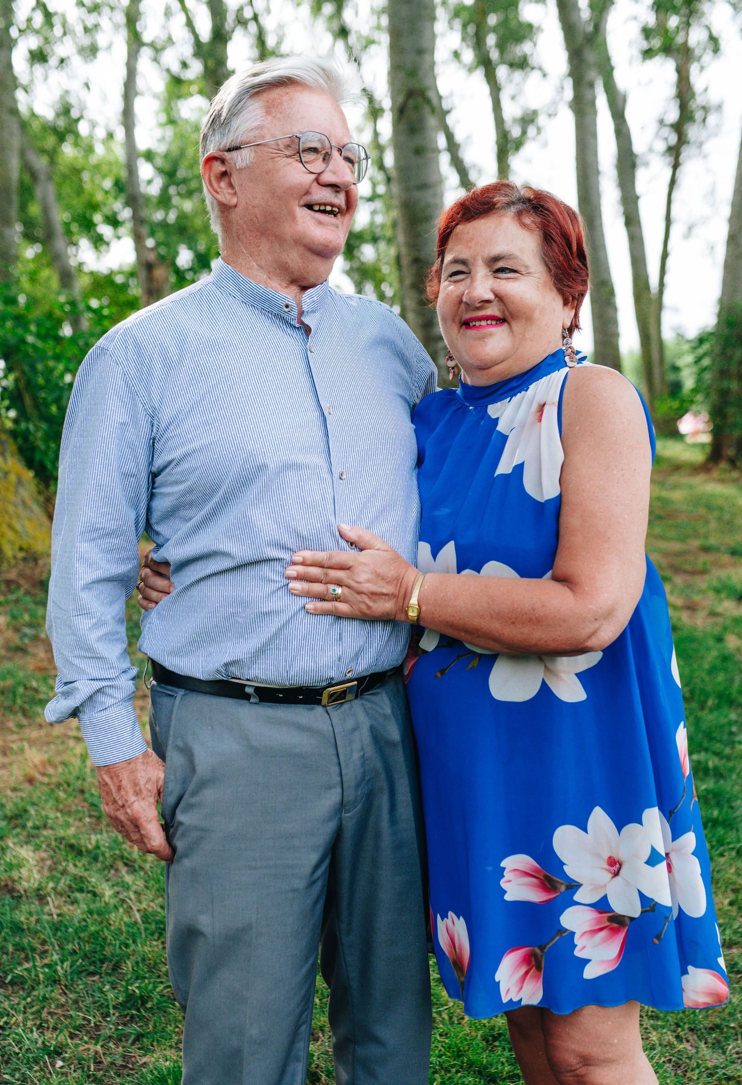 Couple in blue and floral attire sharing joyful moment in garden setting.
