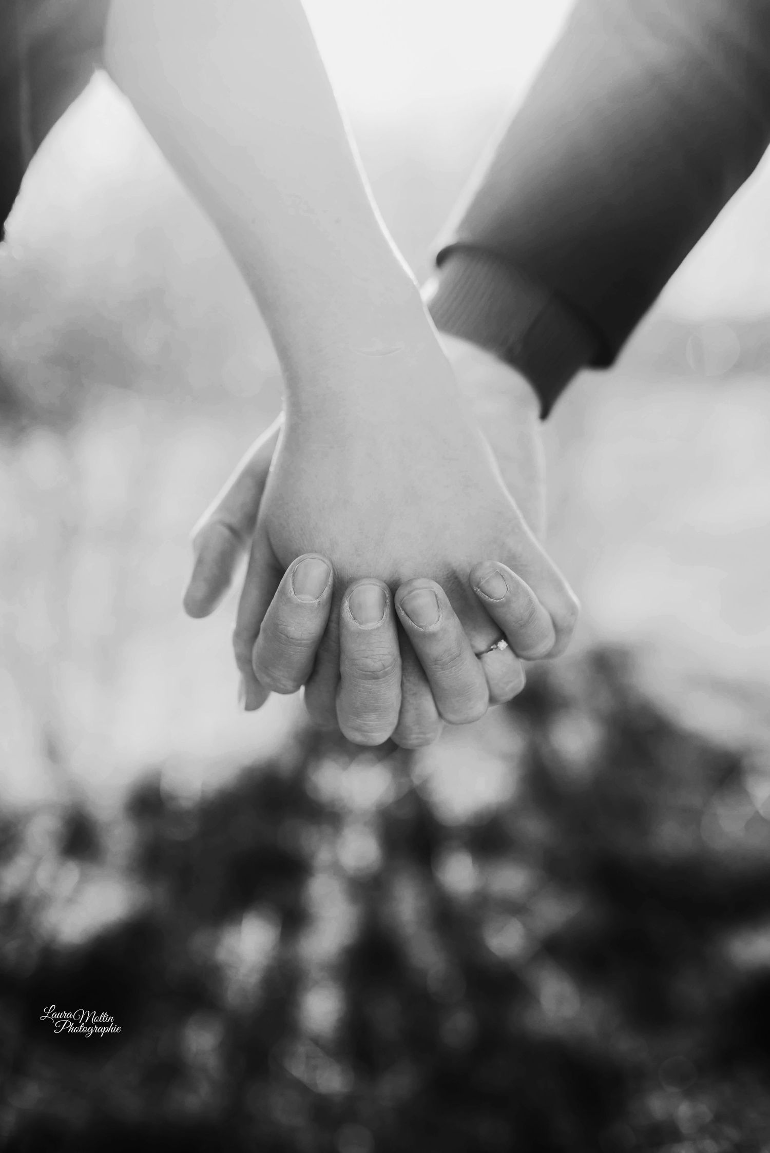 Close-up black and white photo of hands clasped together showing engagement ring.