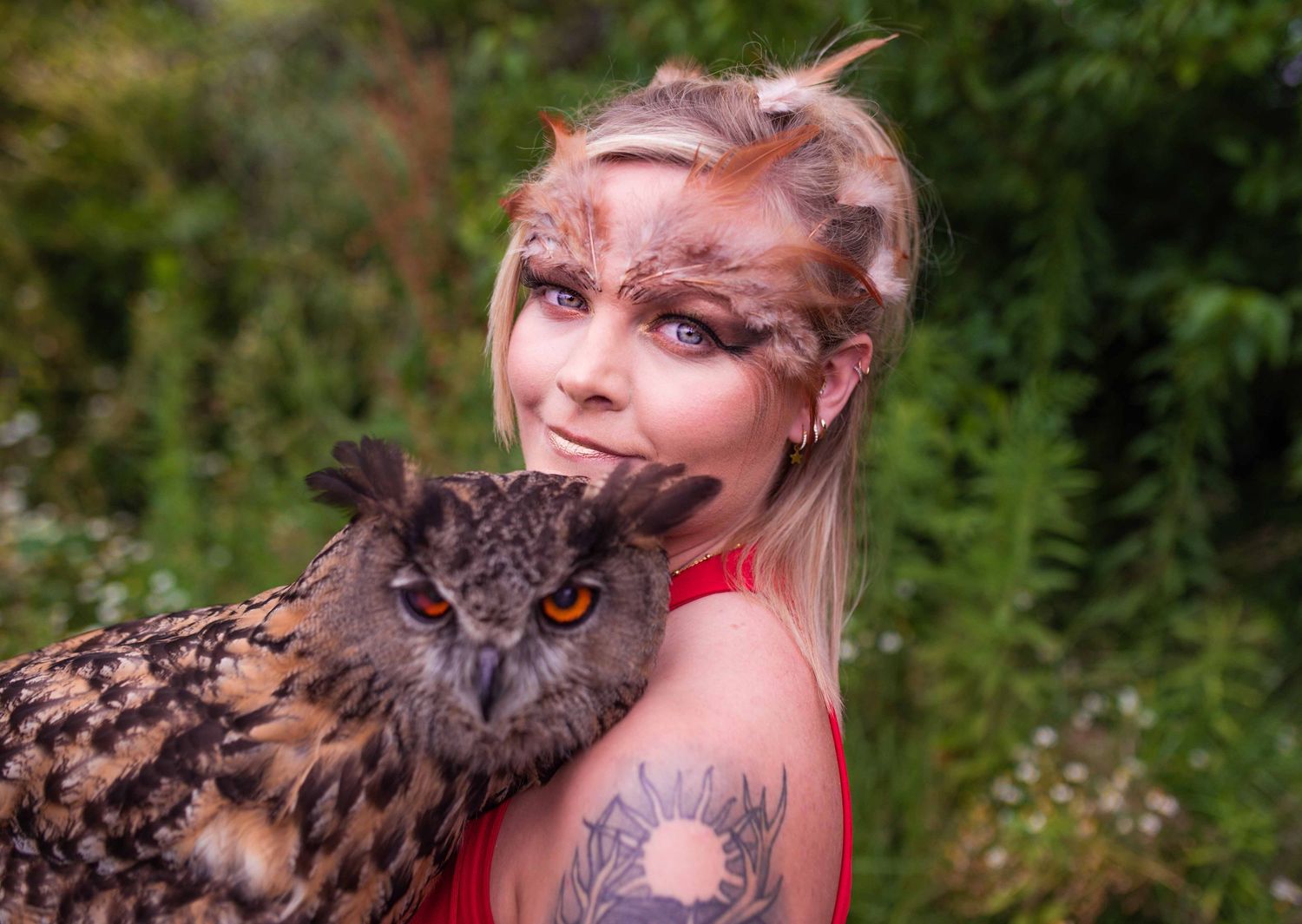 A majestic Eurasian eagle owl perches with its handler in a red dress against a natural outdoor setting.