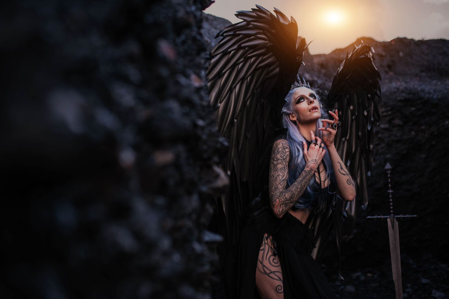 A dramatic silhouette poses with dark wings against a setting sun.