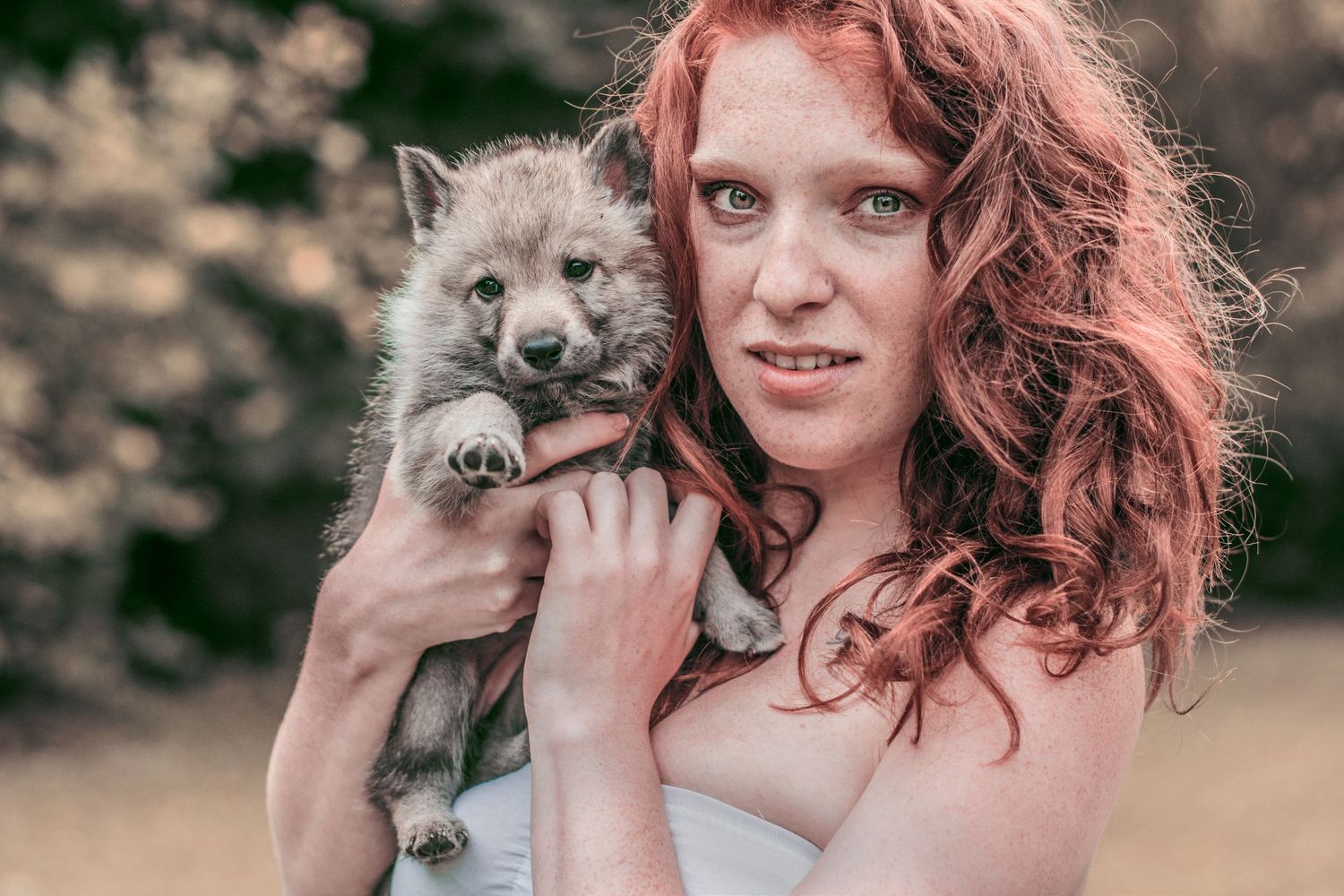 Person with red hair posing with friendly gray husky dog outdoors.