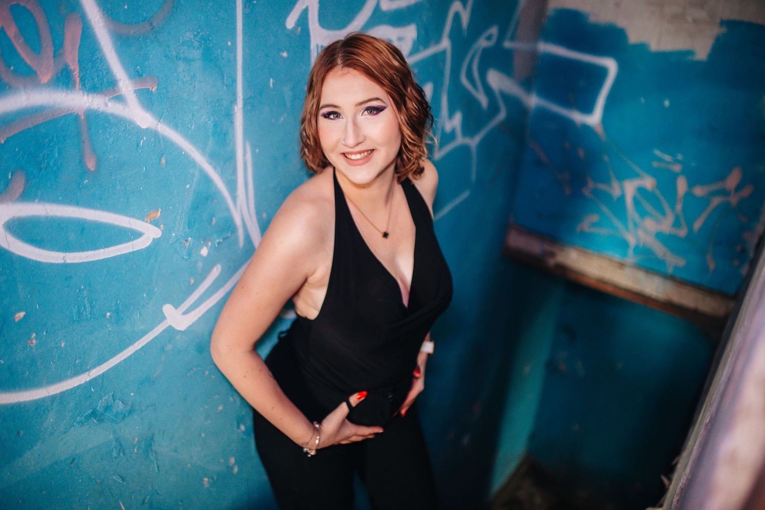 Portrait against blue graffiti wall wearing elegant black dress.