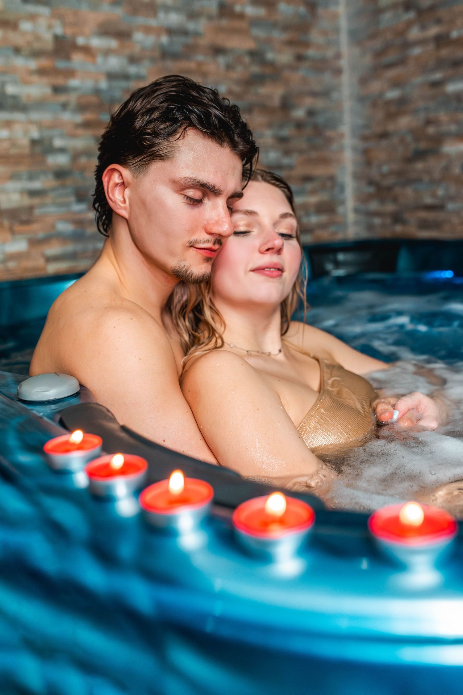 Romantic couple relaxing together in a hot tub jacuzzi with lit candles on the edge.