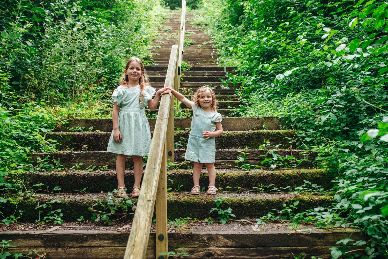 Family enjoying a sunny day outdoors on rustic wooden steps surrounded by lush green foliage.