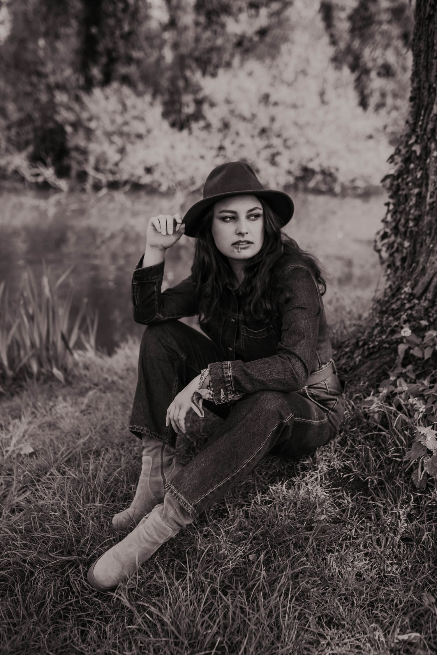 Artistic black and white portrait with a wide-brimmed hat in tall grass.