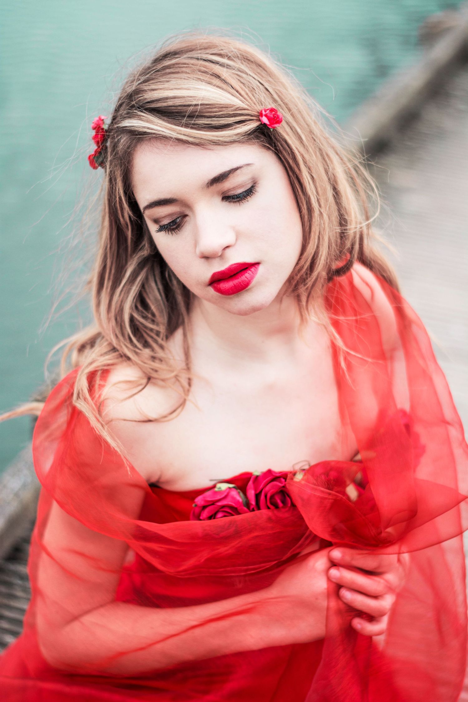 Romantic portrait in a red flowing dress against a teal background.