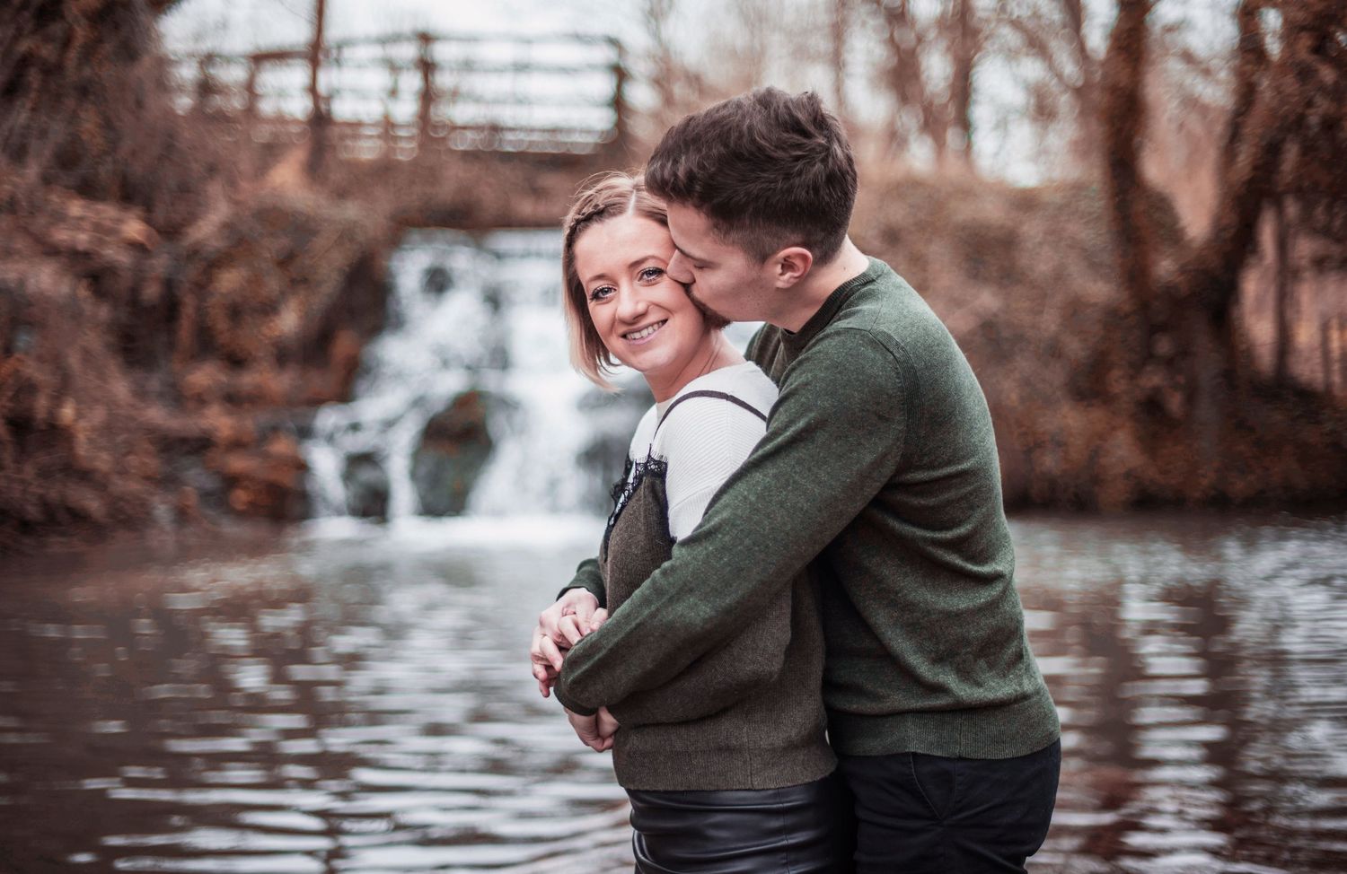 Romantic couple photos by a rustic fence and water feature in warm tones.