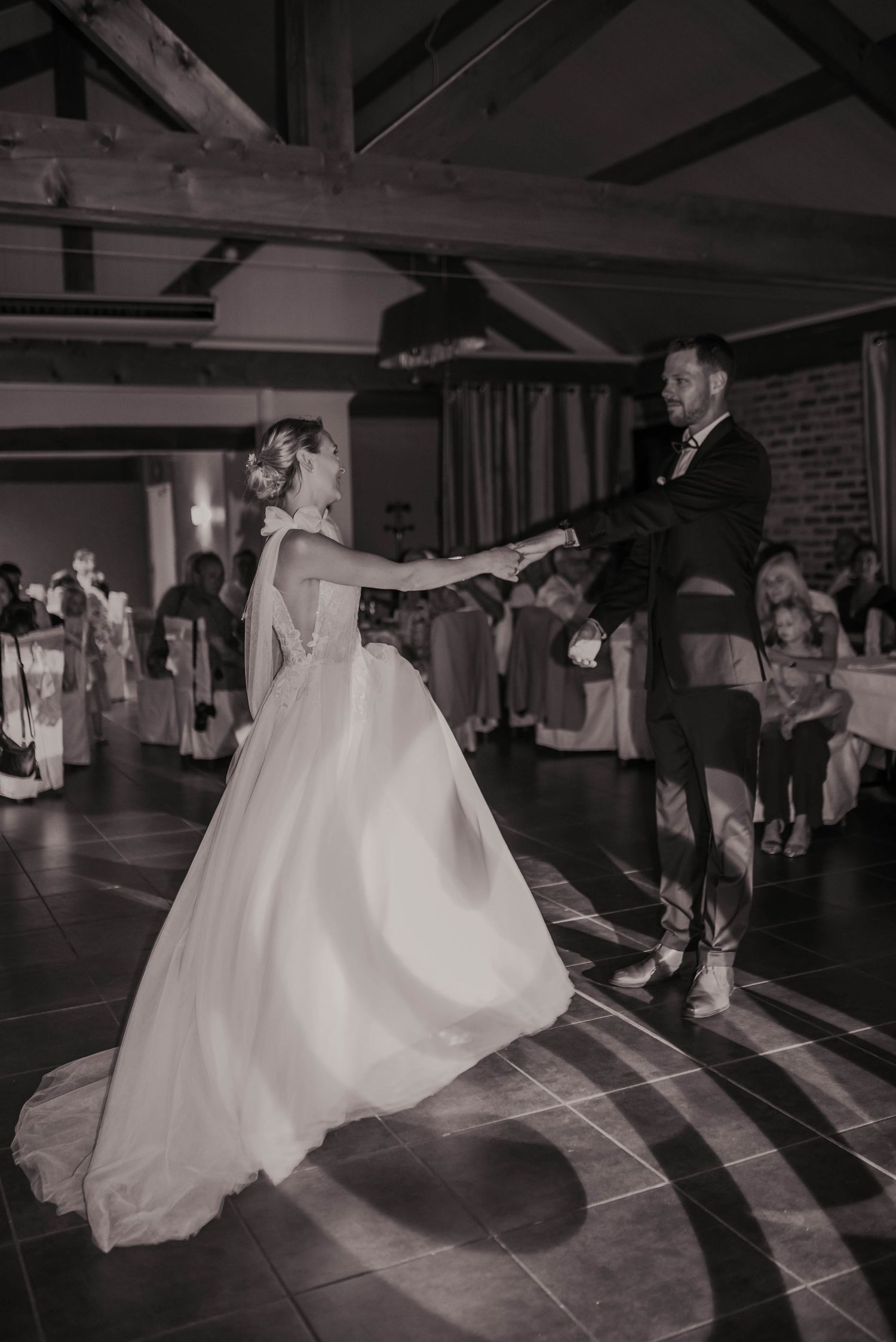 Black and white photo of wedding couple dancing in a rustic indoor reception venue.