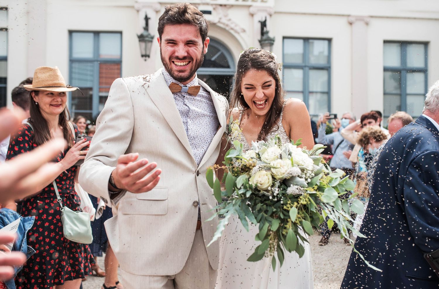 Wedding guests celebrate with confetti outside a white building.