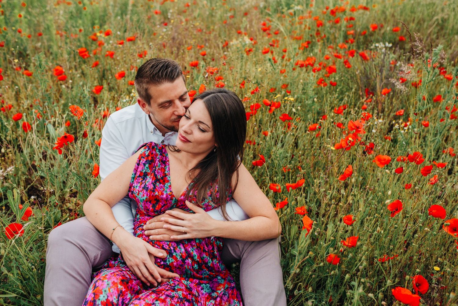 Romantic engagement session in field of wild red poppies during golden hour.
