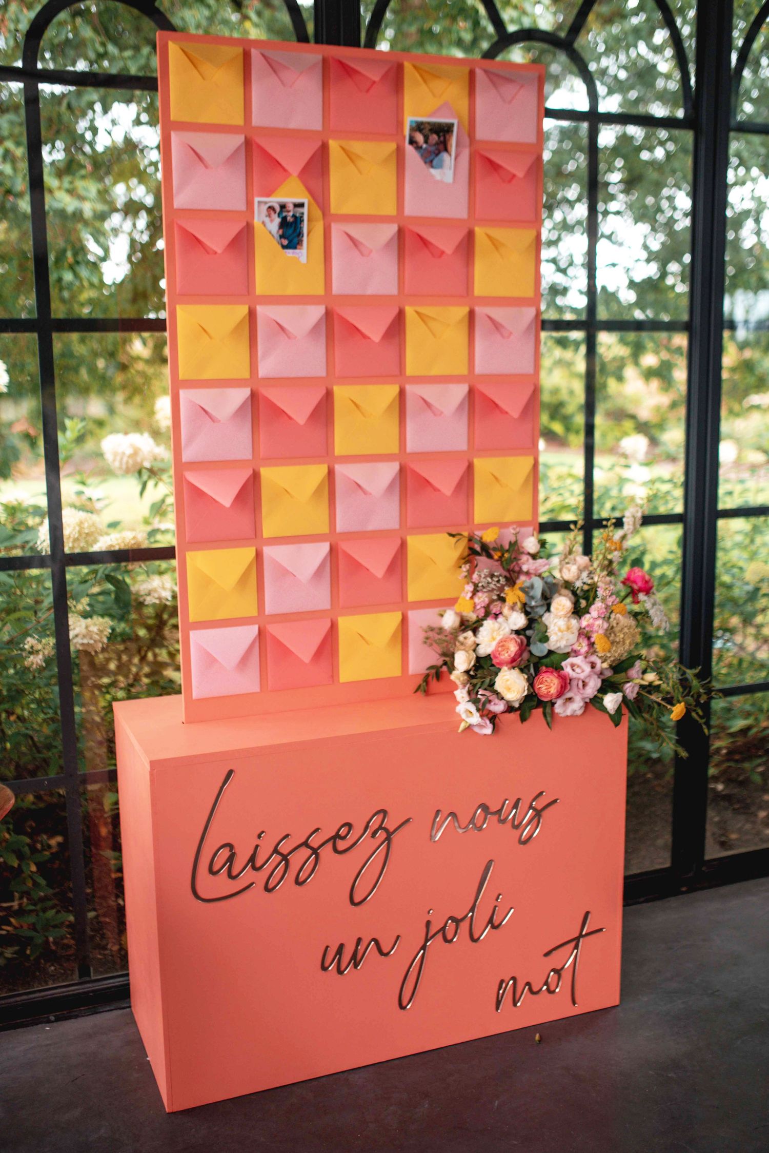 Coral and peach geometric paper wall art display with French text at wedding venue.