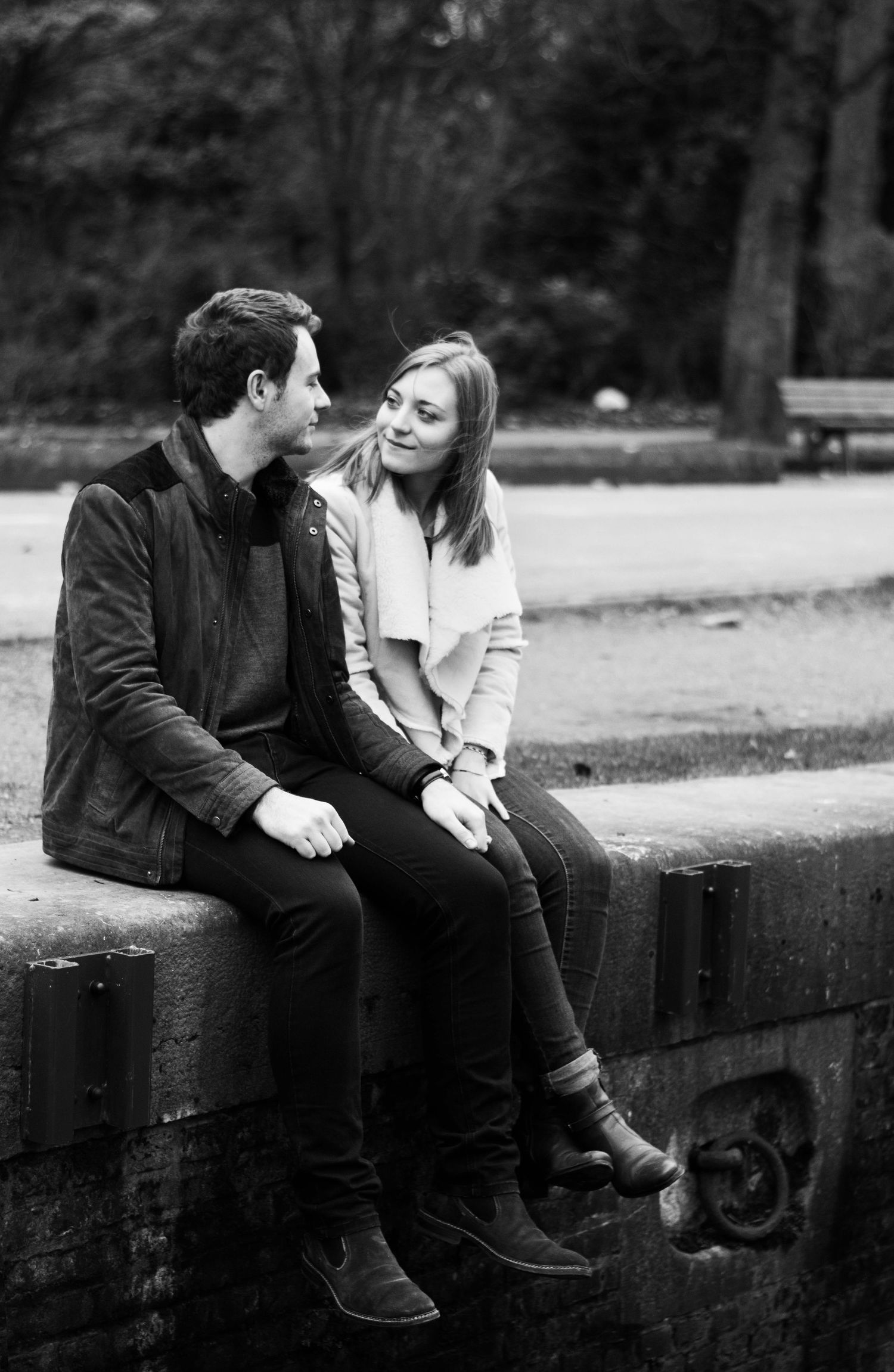 Black and white photo of couple sitting on concrete wall in casual setting.