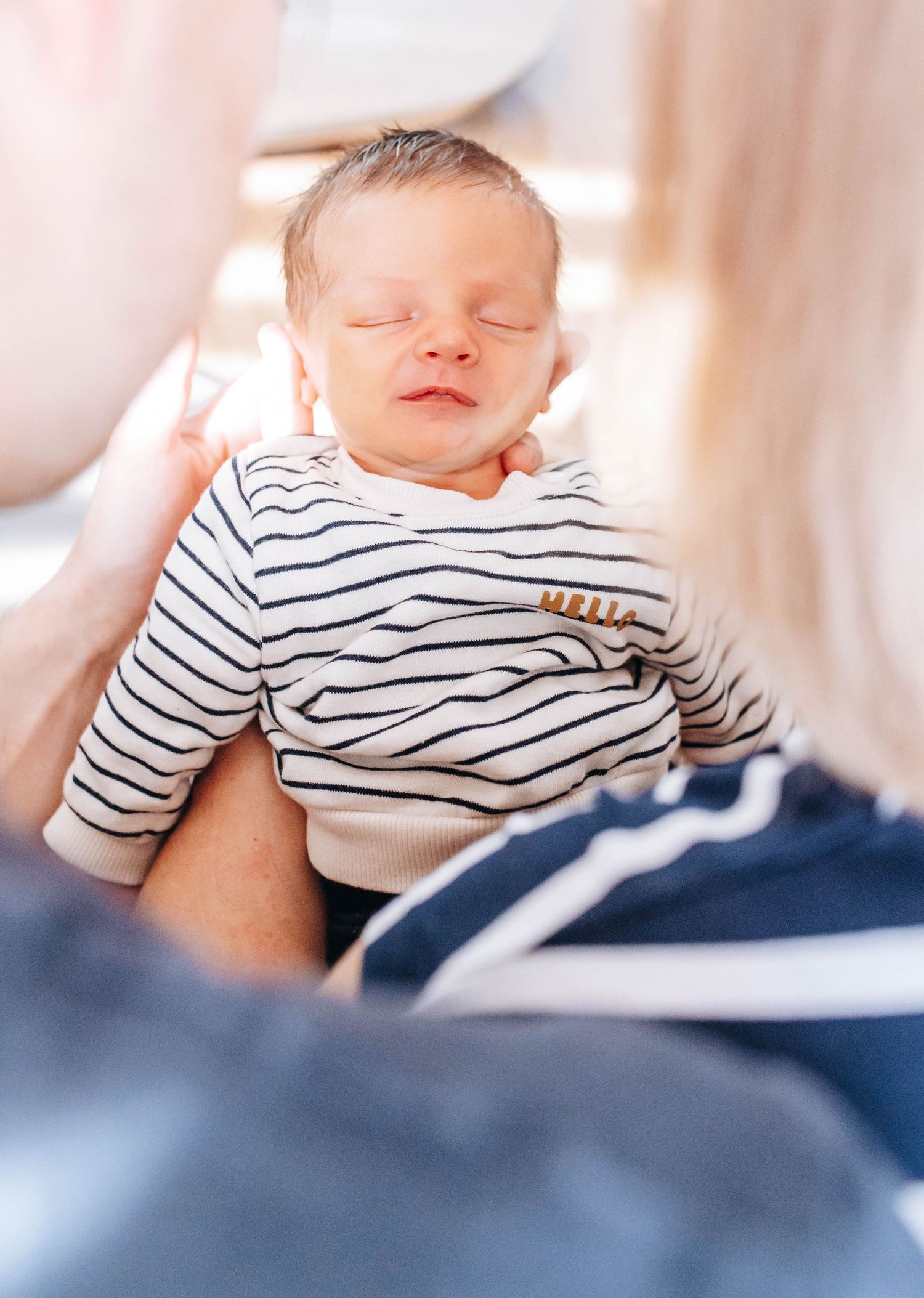 Newborn baby sleeping peacefully in striped onesie, cradled in parents arms during a professional newborn photo session.