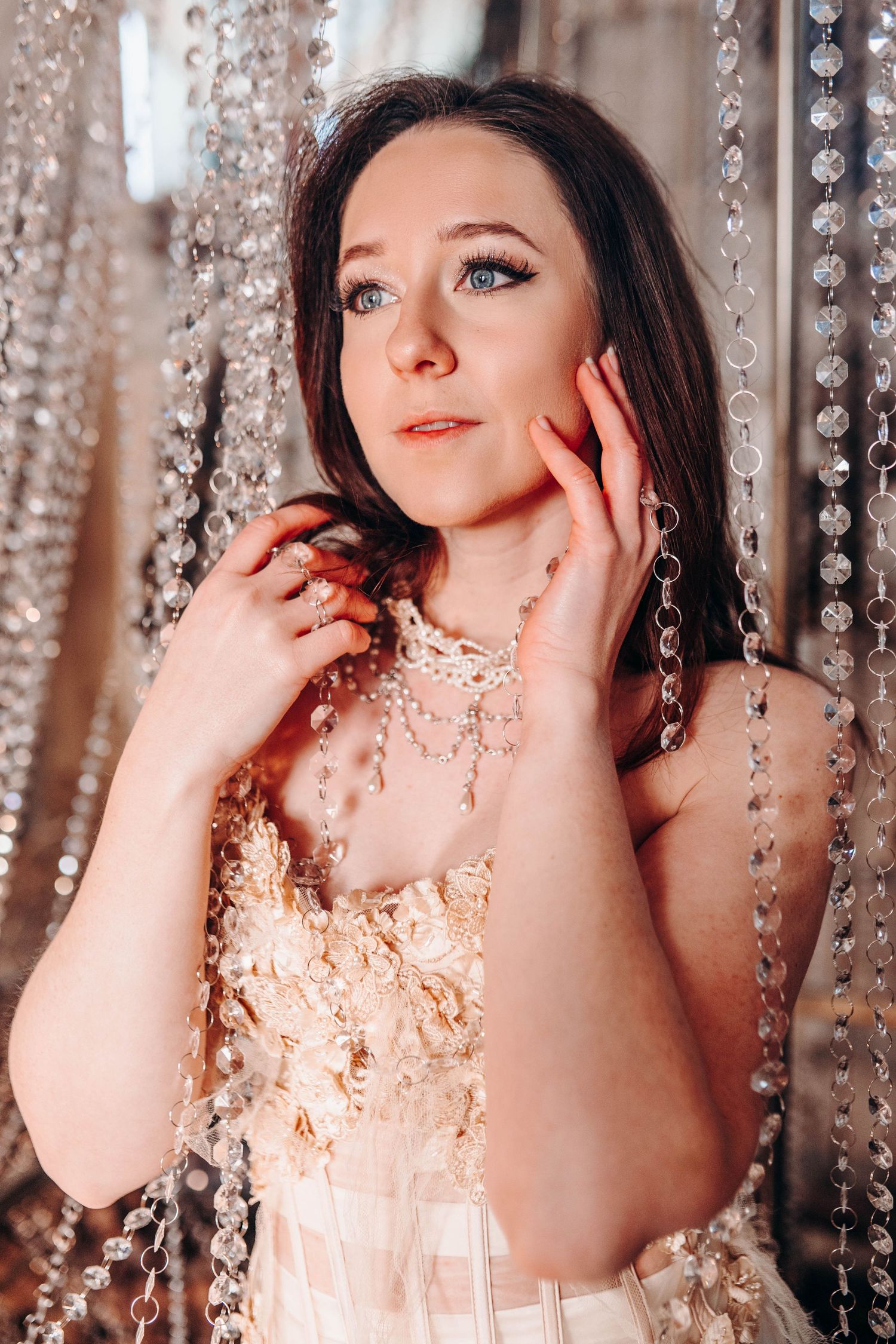 Young woman in beaded gown poses gracefully against sparkling crystal bead curtain backdrop.