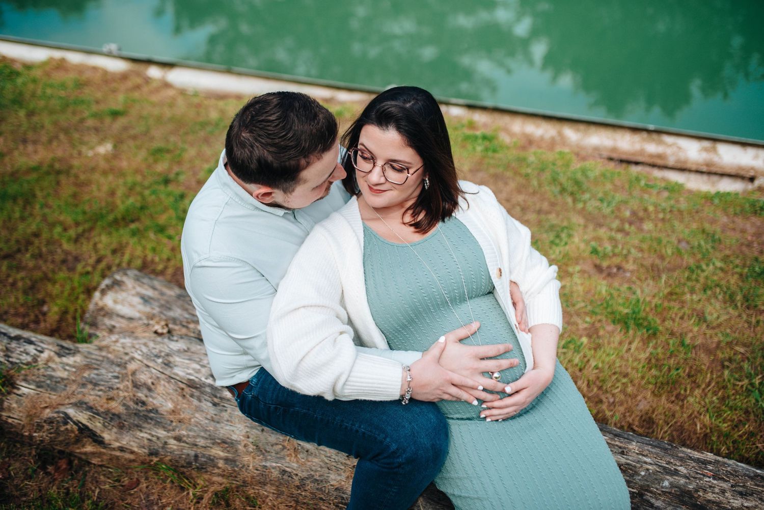 A couple shares an intimate moment during their maternity photoshoot by a lake.