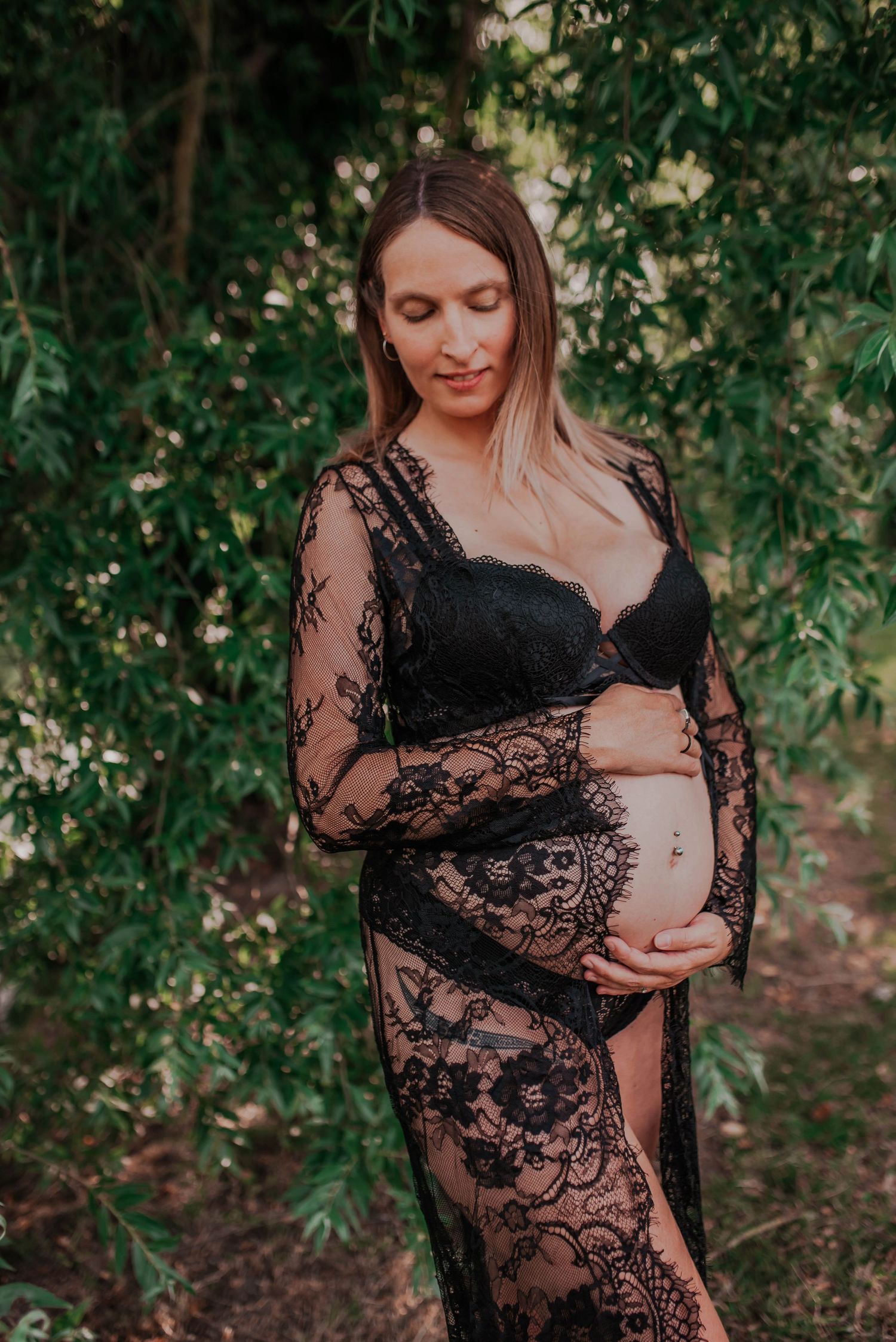 Artistic maternity photos in black lace against a natural forest backdrop.