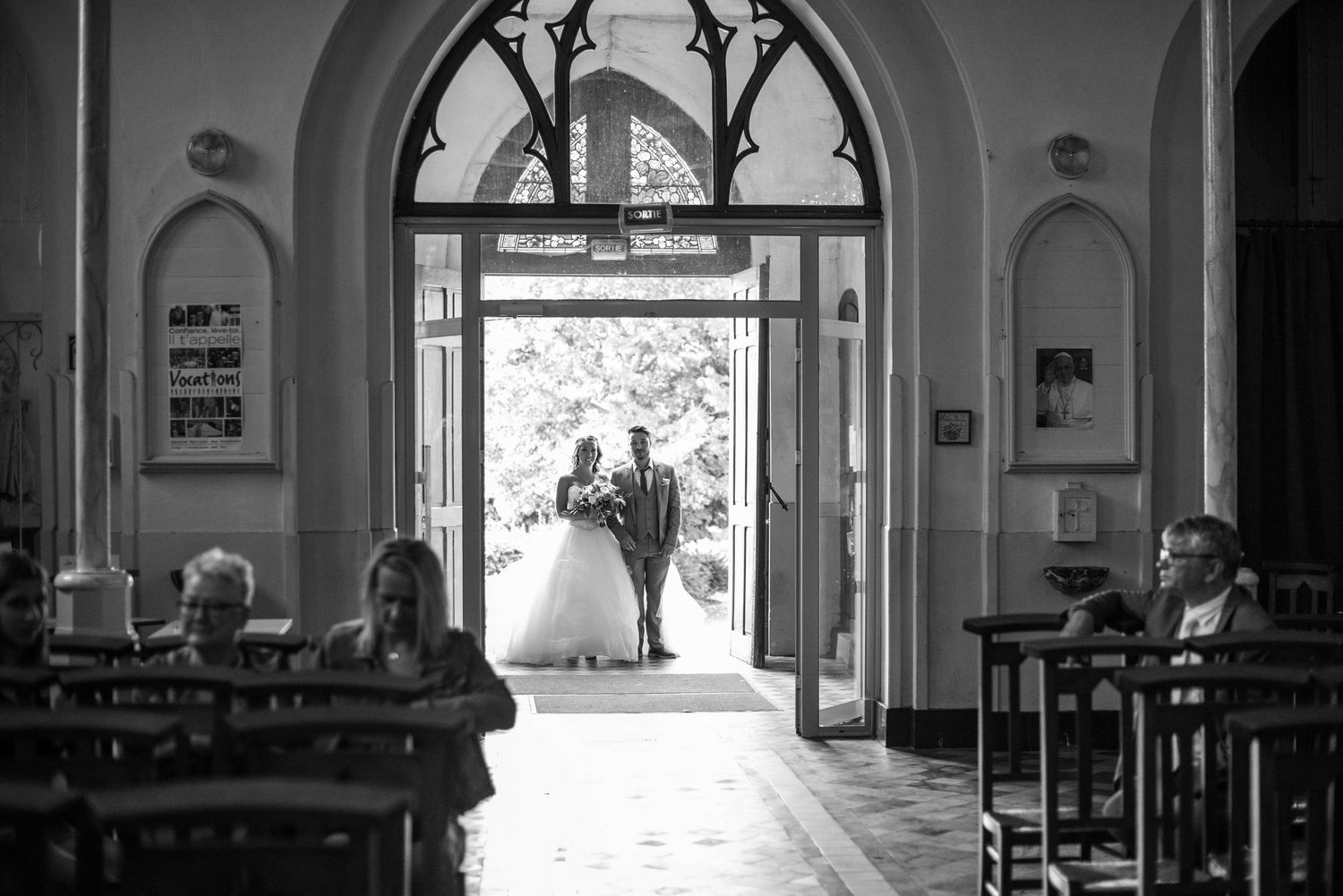 A wedding ceremony silhouette through an ornate church doorway in black and white.