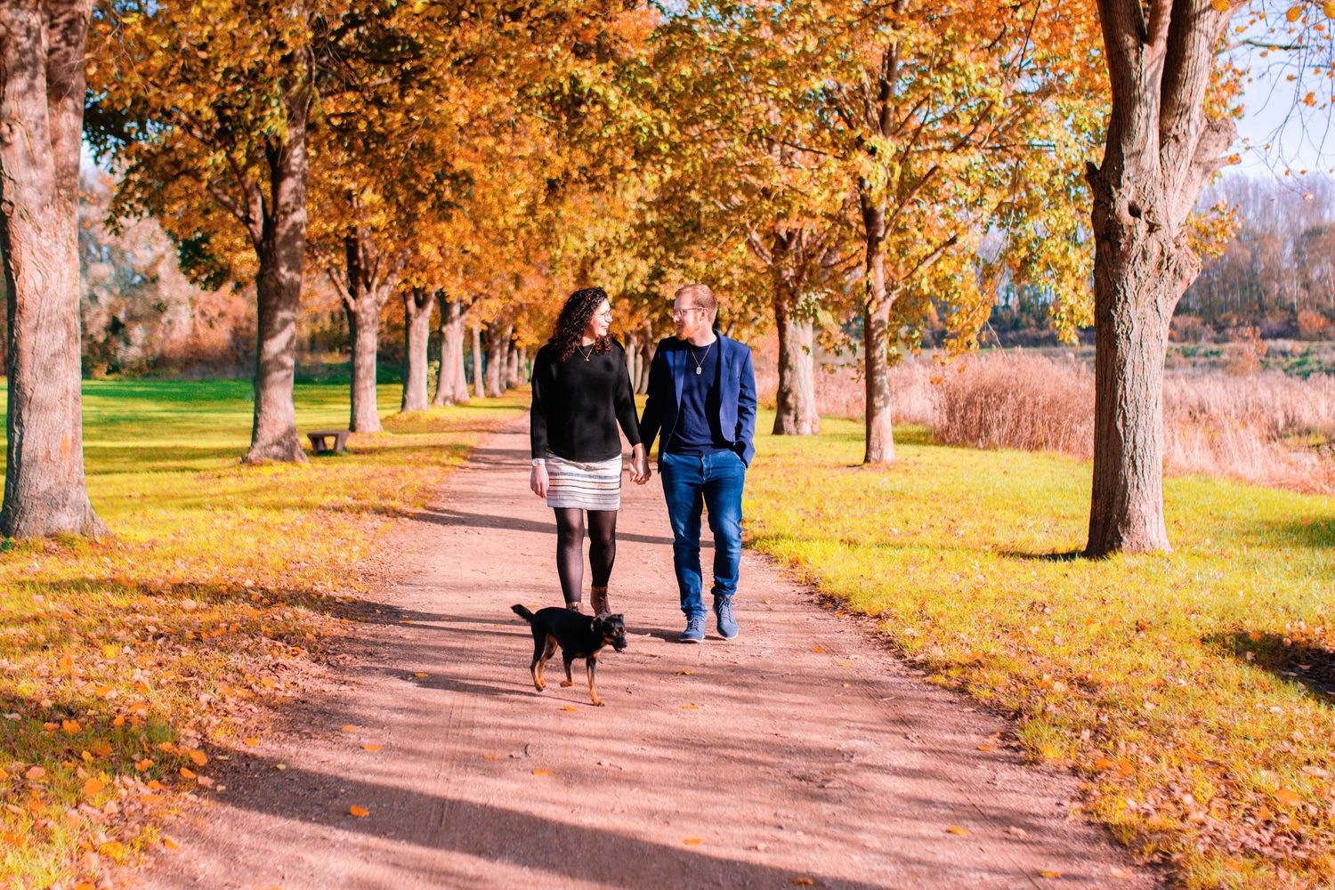 People walking along a tree-lined path with golden autumn foliage.