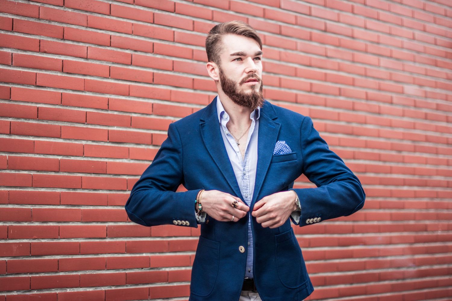 Man in blue suit demonstrates dynamic poses against brick wall.