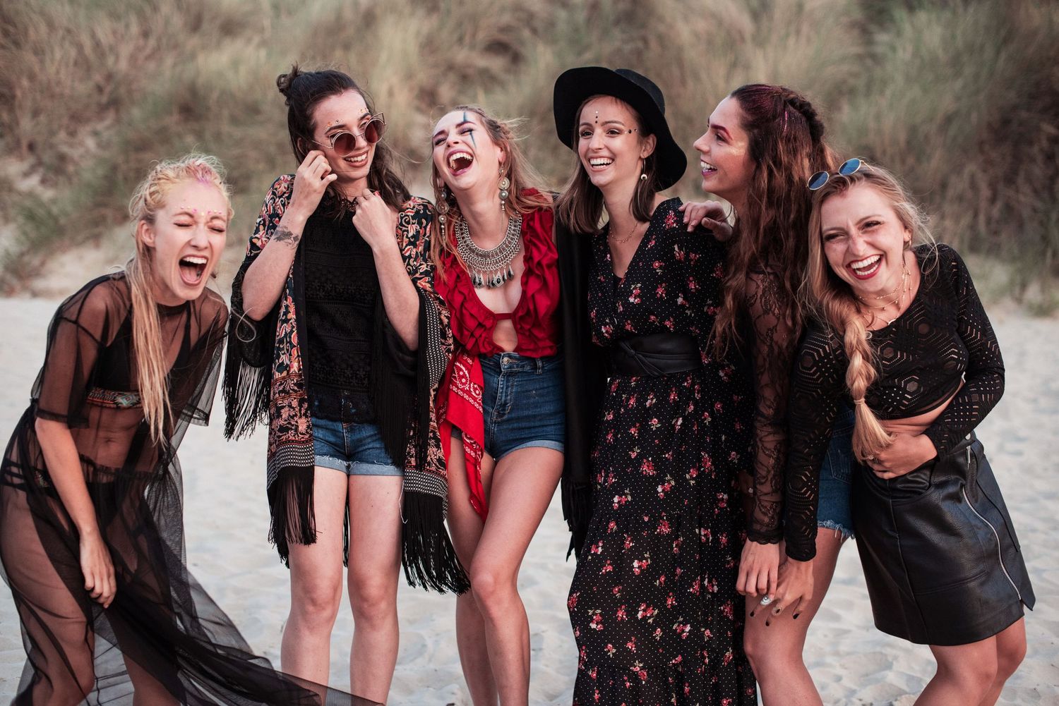 Friends posing and laughing together during beach photoshoot in casual attire.