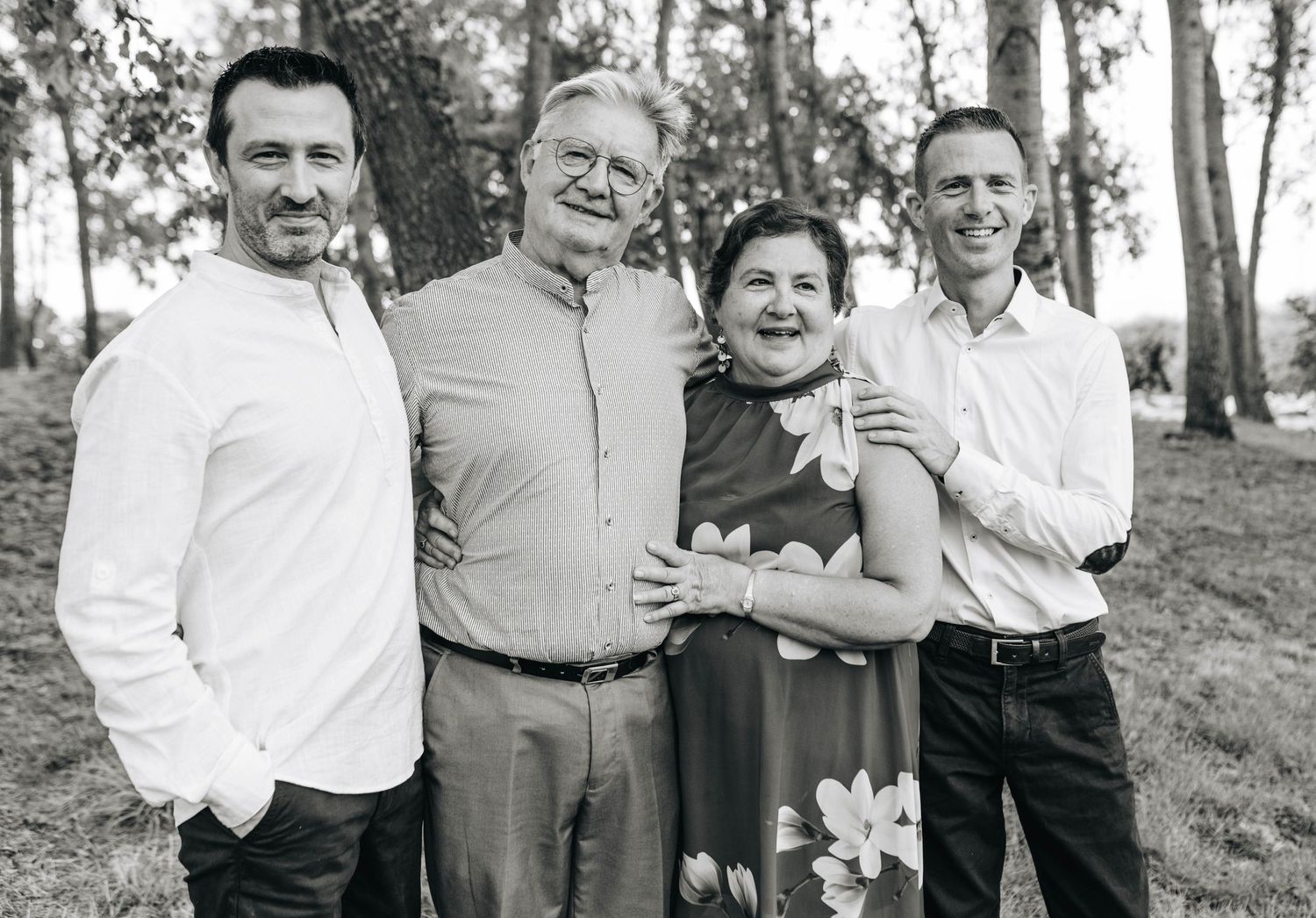 Black and white portrait of family members standing together outdoors among trees.