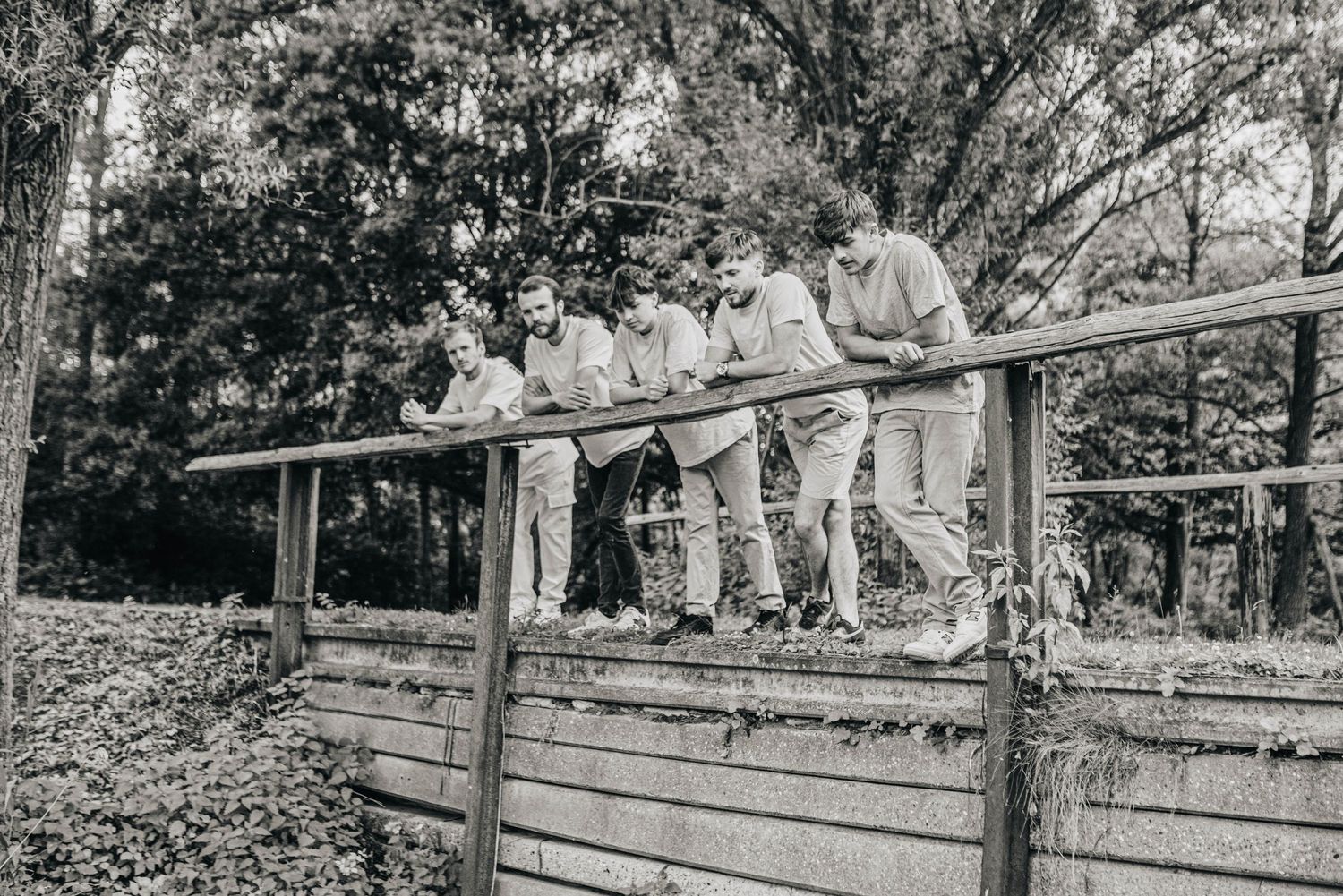 Black and white image of people sitting and standing on wooden bleachers outdoors.