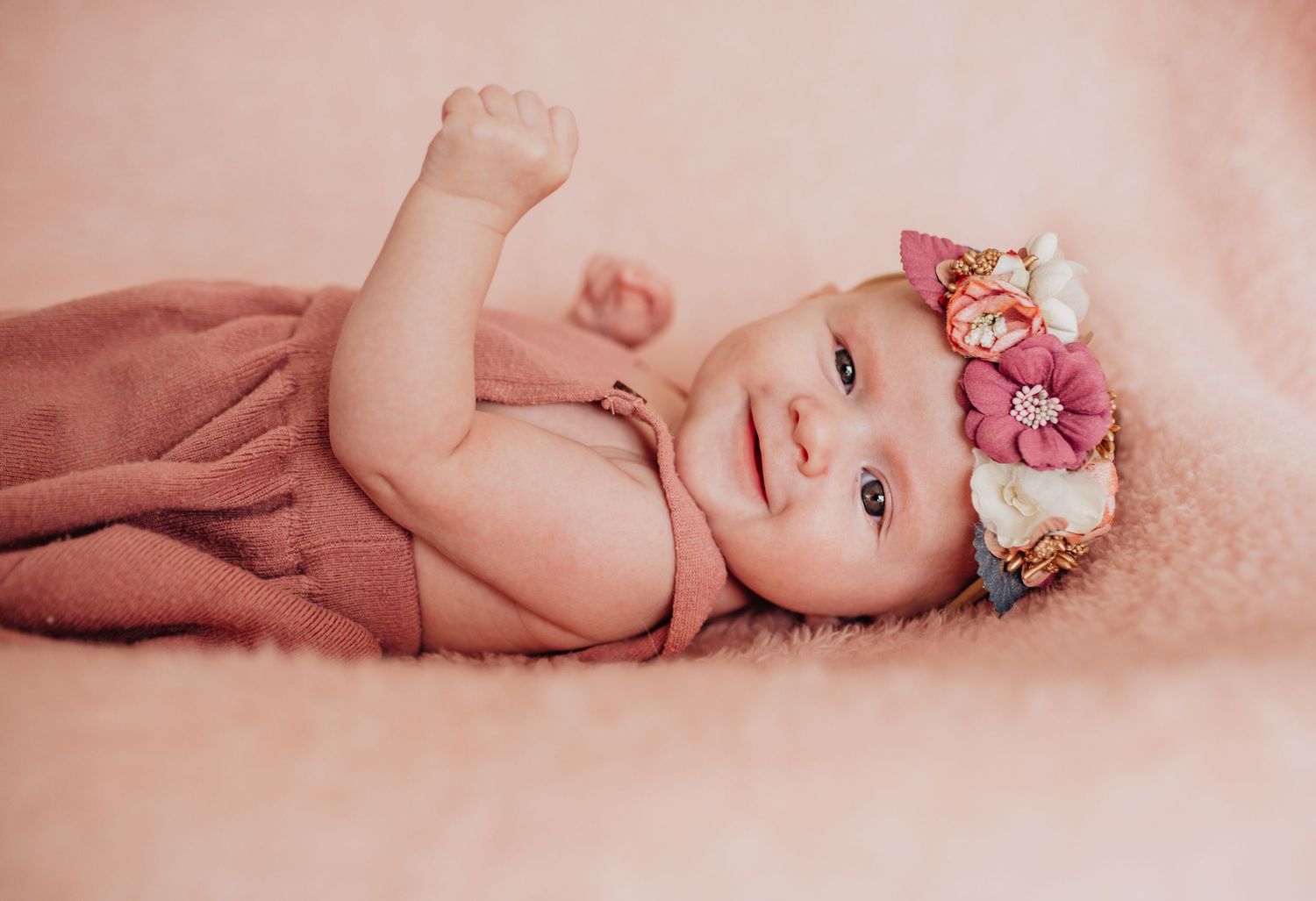 Newborn baby rests peacefully on pink backdrop with floral accessories.