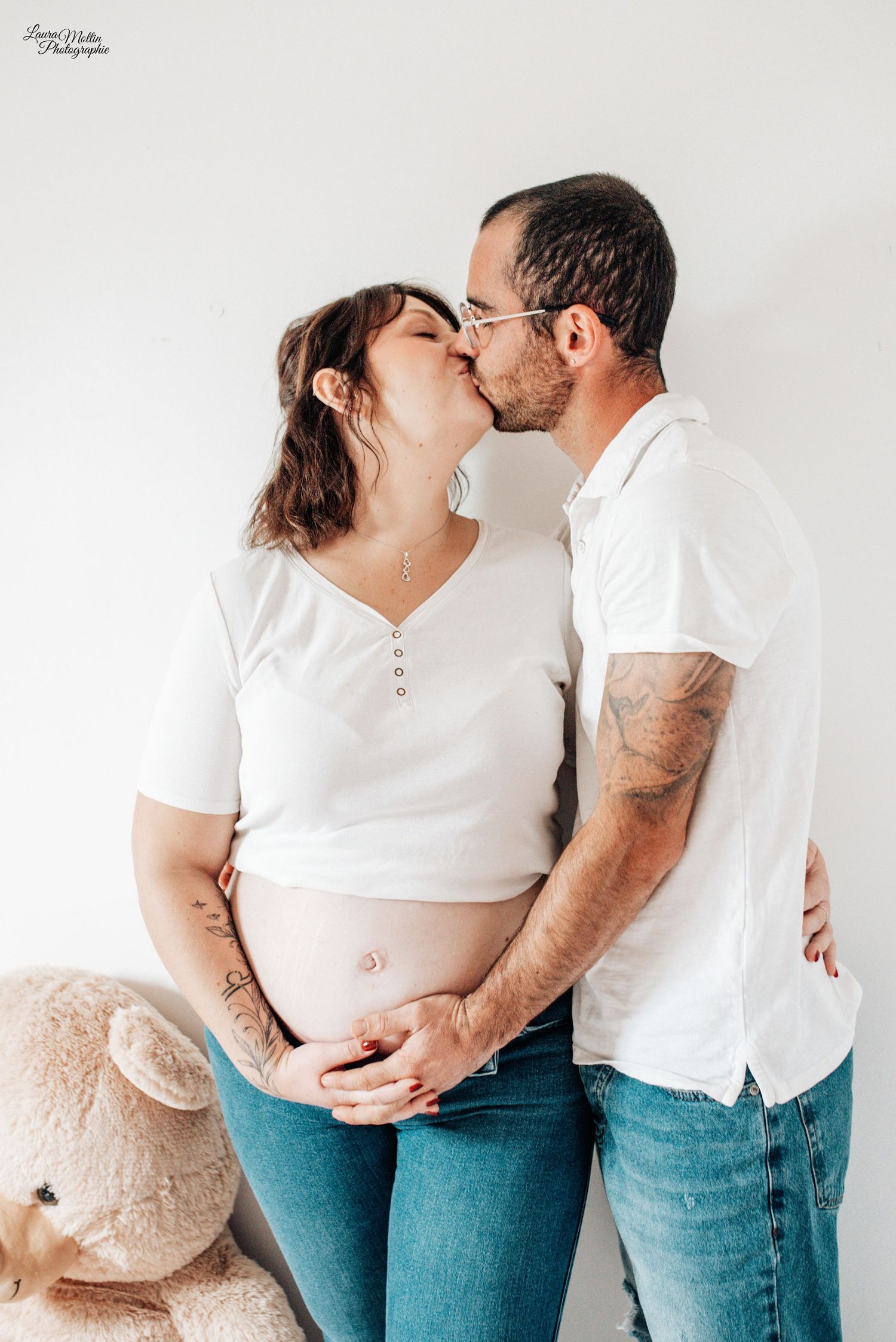 Intimate maternity photoshoot with couple in white and denim against white background.