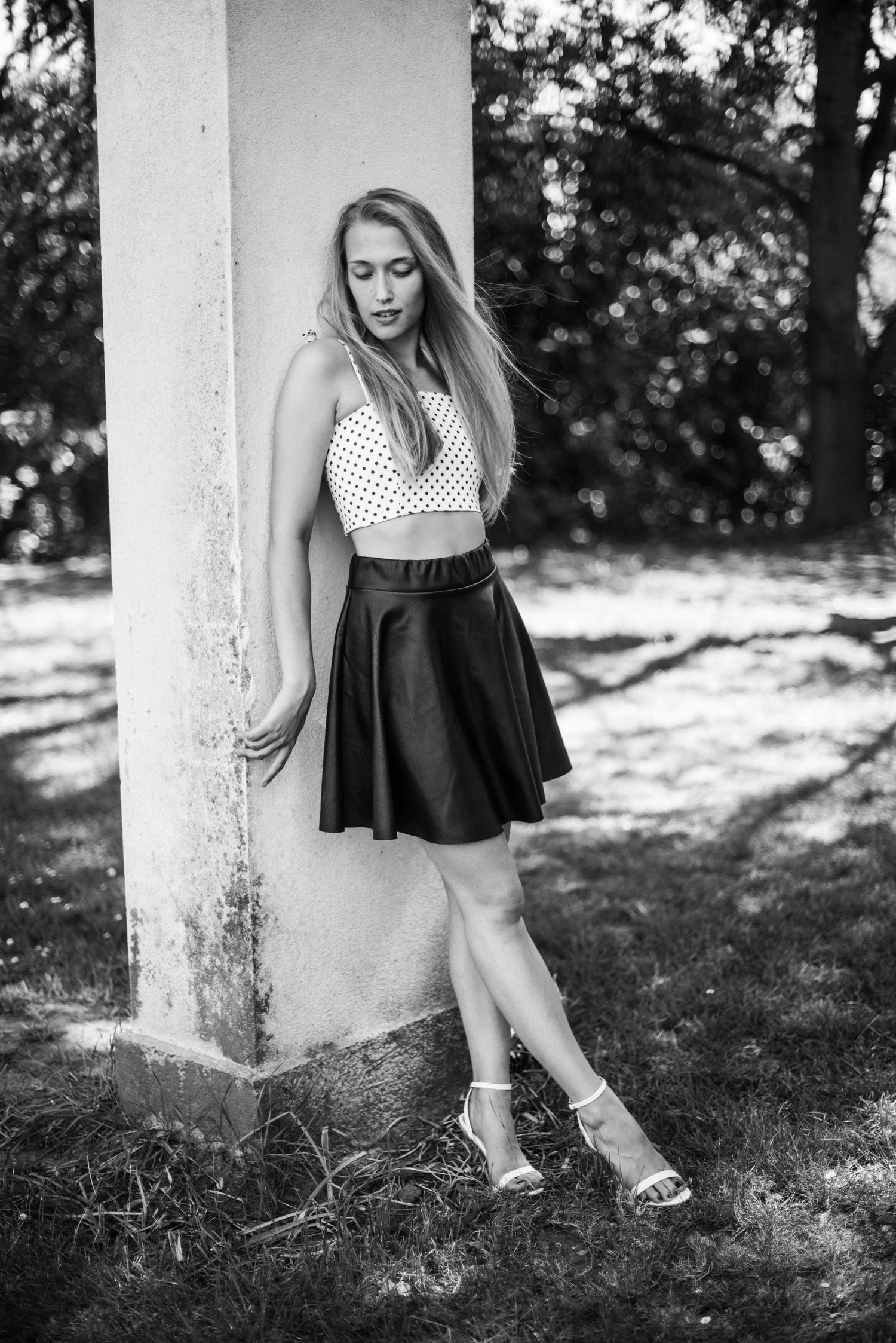 Black and white portrait in polka dot top and skirt leaning against white column.