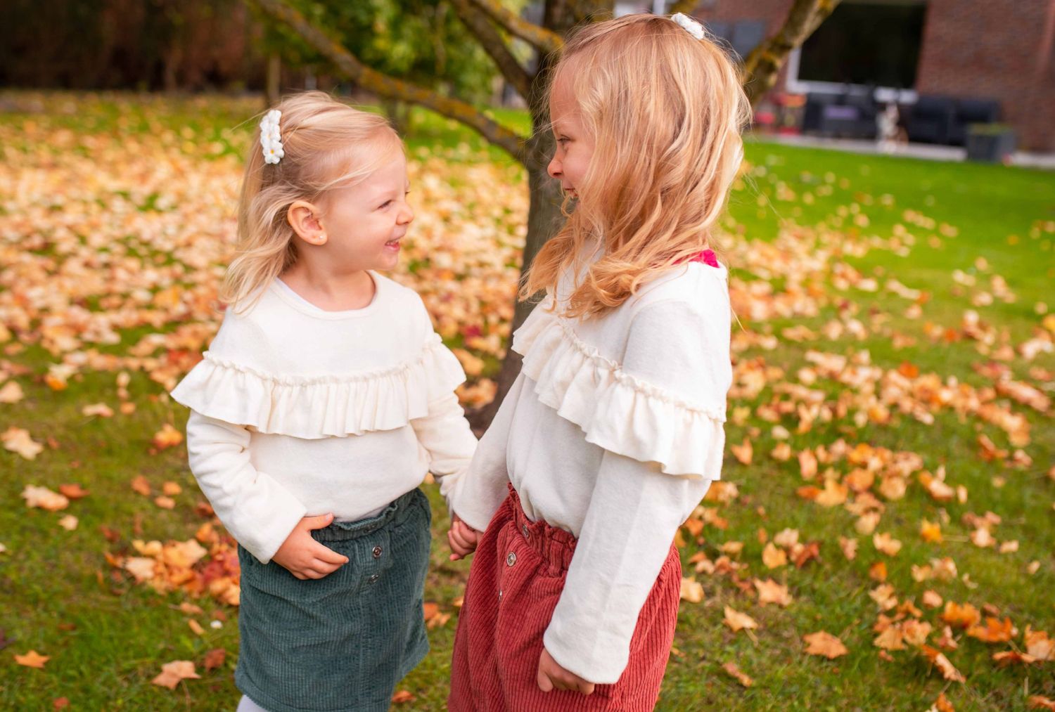 Children in autumn outfits playing among fallen leaves.