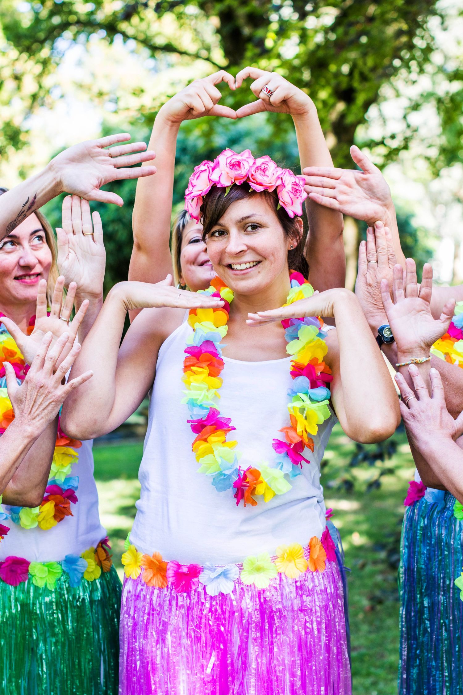 Group wearing colorful Hawaiian leis and grass skirts poses with playful hand gestures.