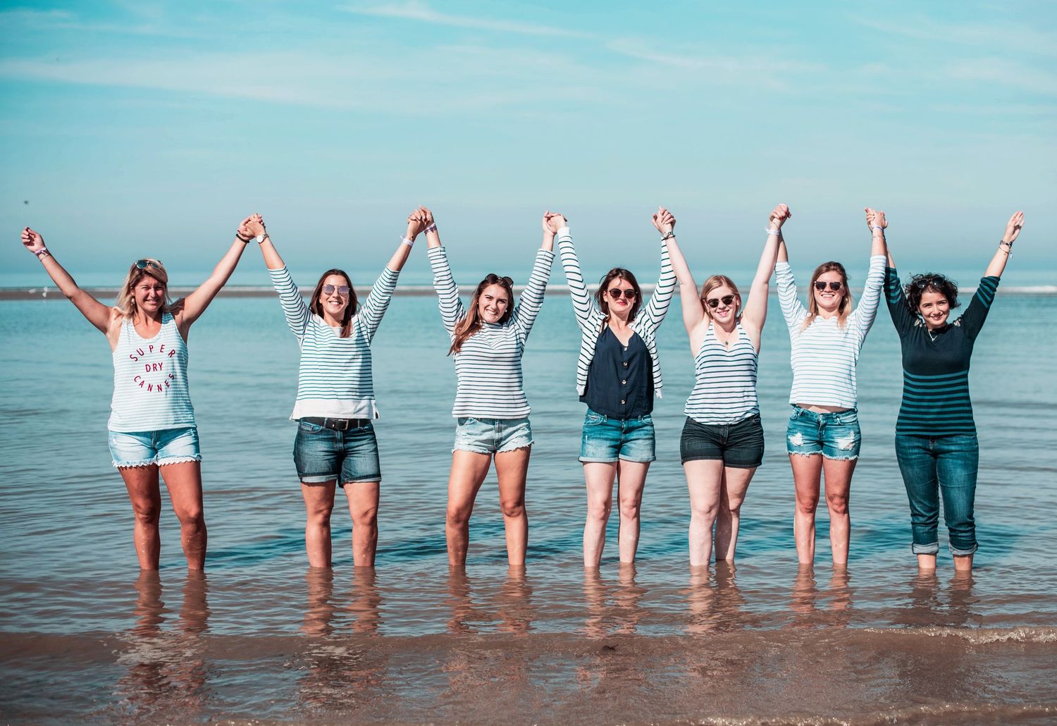 Friends stand in ocean water with raised arms against blue sky backdrop.