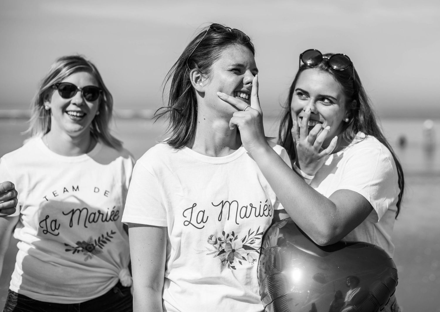 Group of friends wearing matching white t-shirts laughing together at the beach.