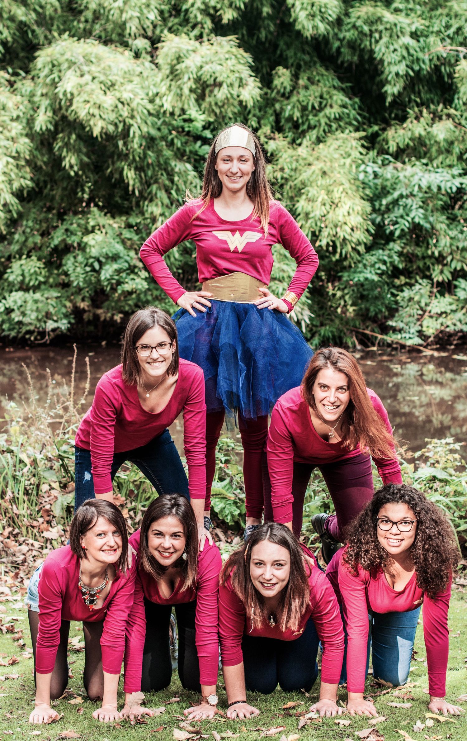 Group in matching burgundy tops forms playful human pyramid outdoors.