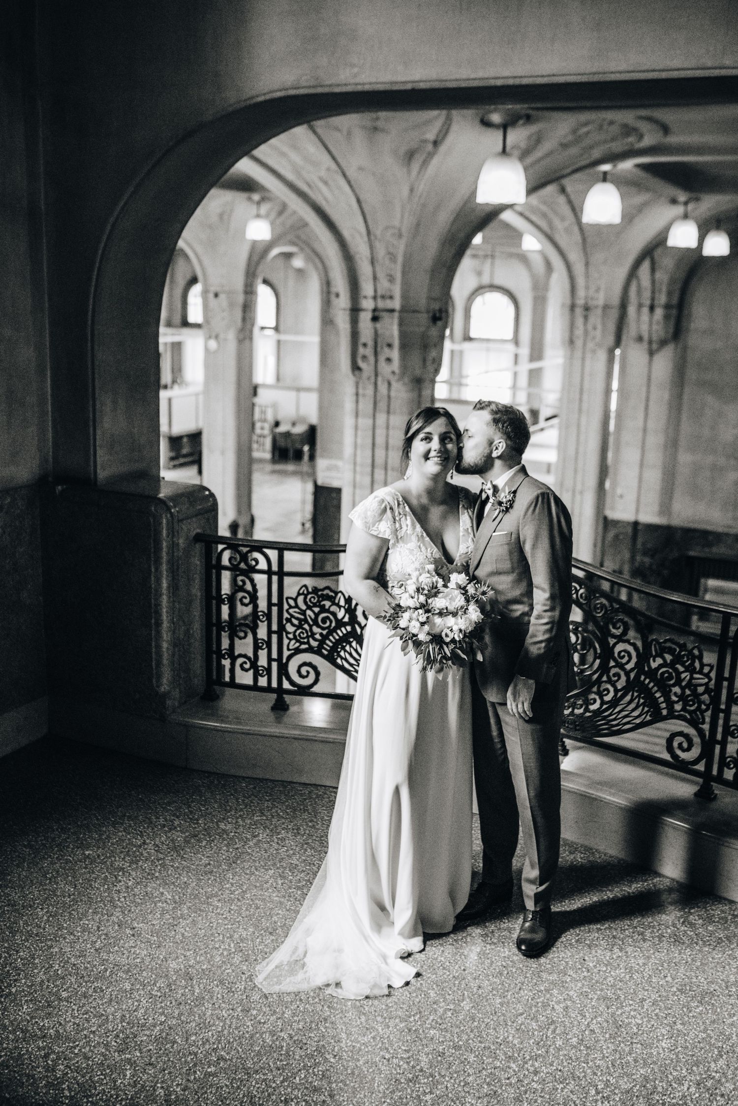 Romantic black and white portrait under arched hallway with ornate iron railings.