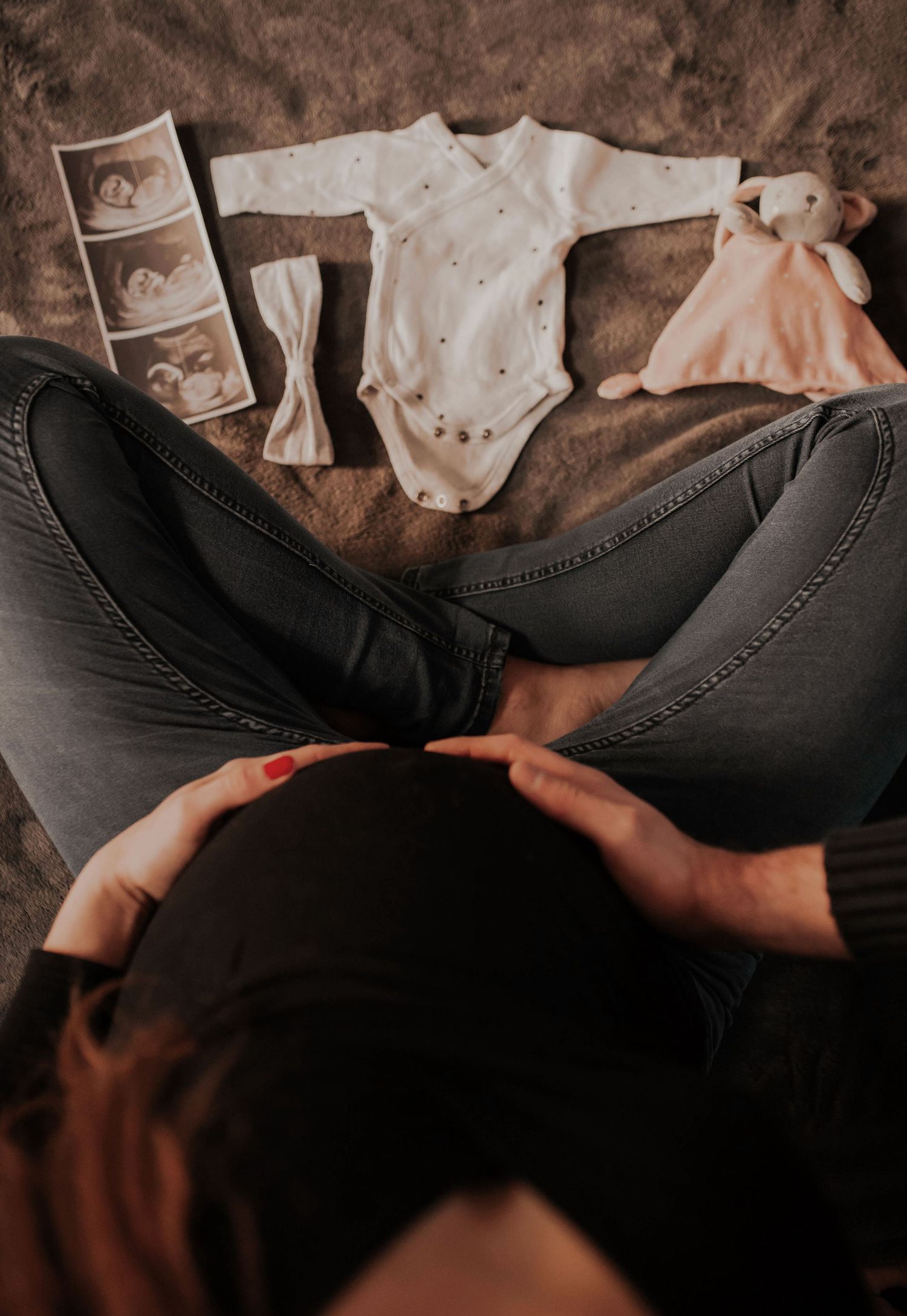 Baby clothes and ultrasound photos laid out with pregnant belly visible below.