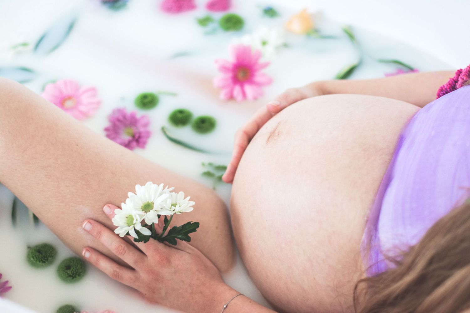 Artistic maternity photo with flowers arranged around a pregnant belly against white background.