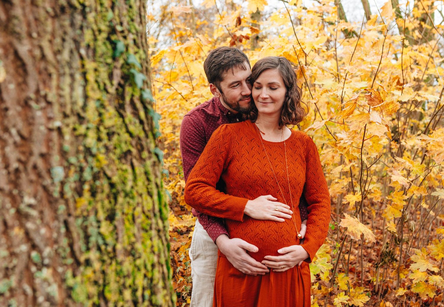 Maternity photoshoot in a wooded area with golden autumn colors.
