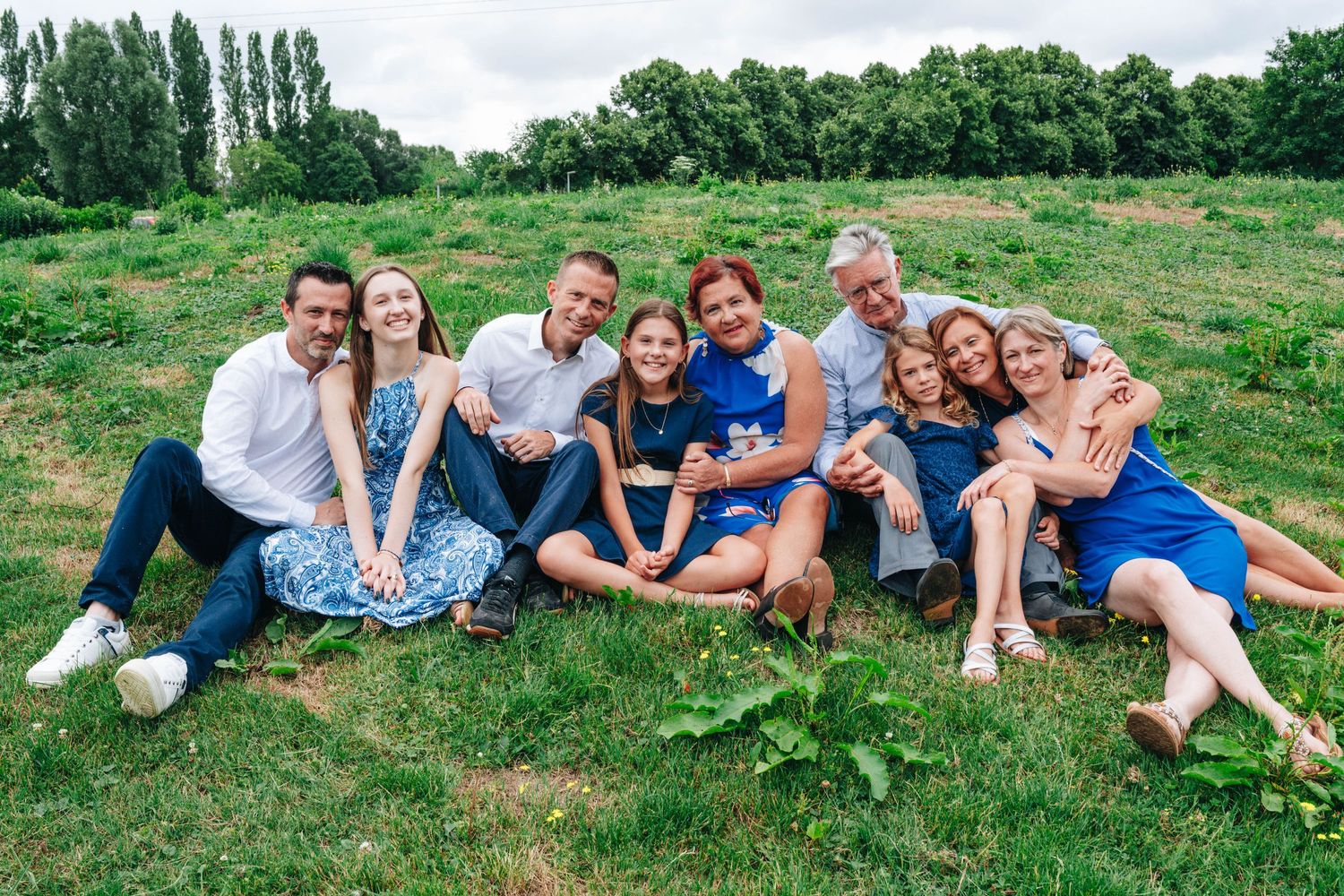 Large family group relaxing on grass during summer photoshoot in park setting.