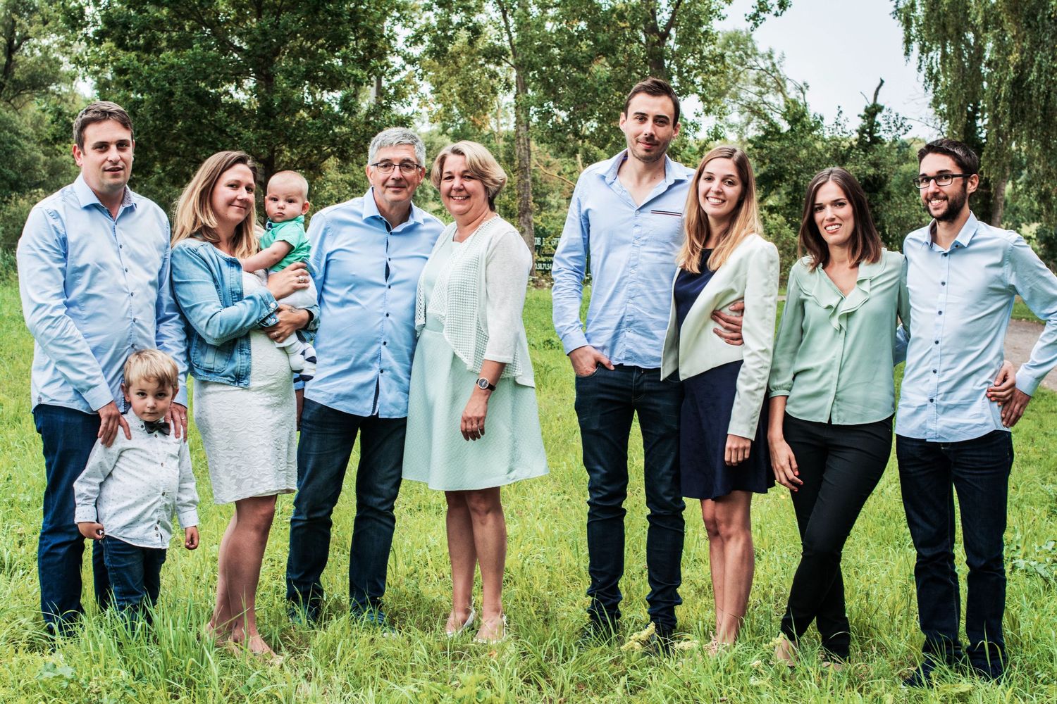A multi-generational family group poses together outdoors wearing coordinated blue and white outfits.